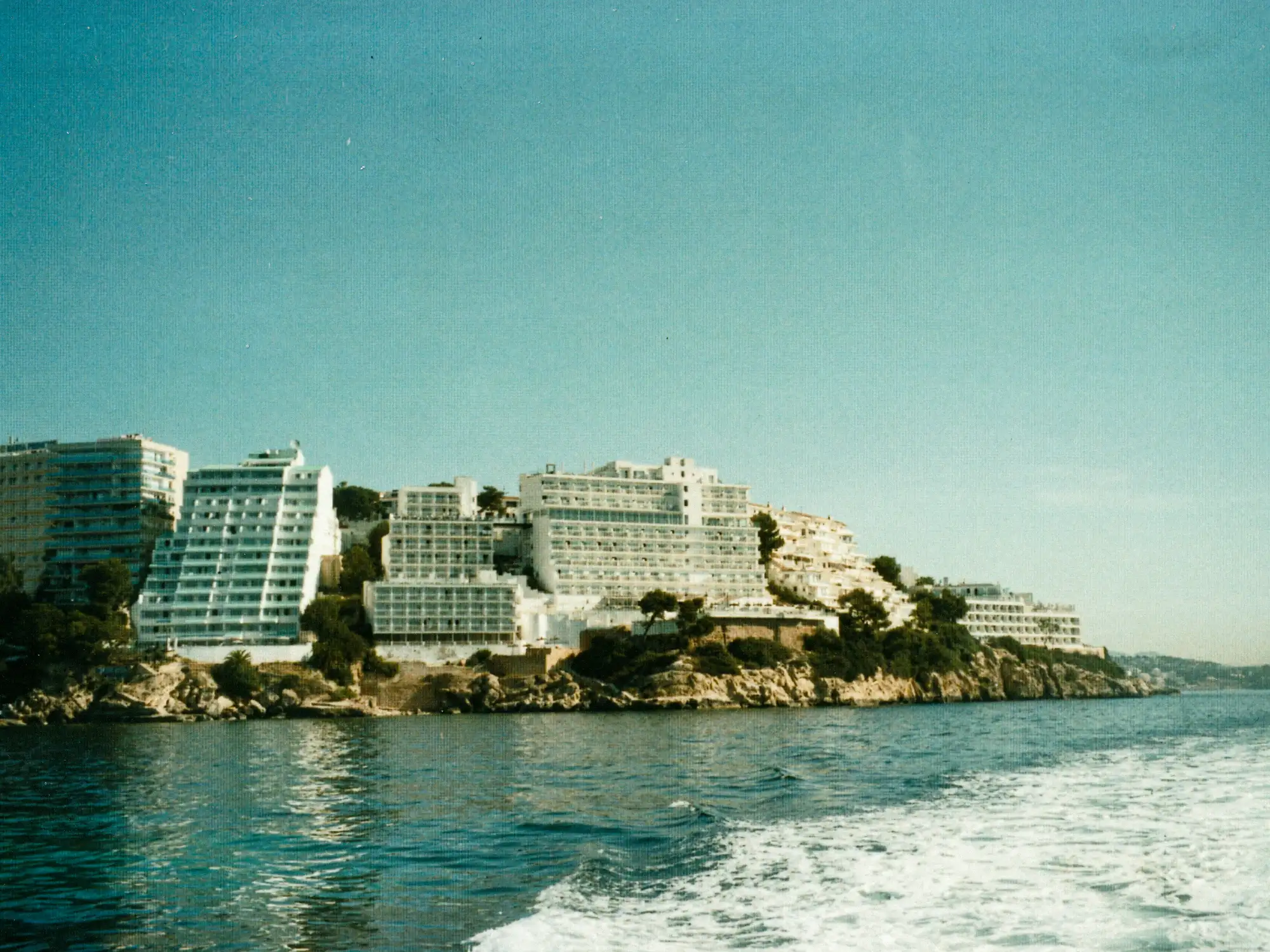 Blick von der fahrenden Yacht auf eine felsige Insel und die weiße Heckwelle vor Mallorca.
