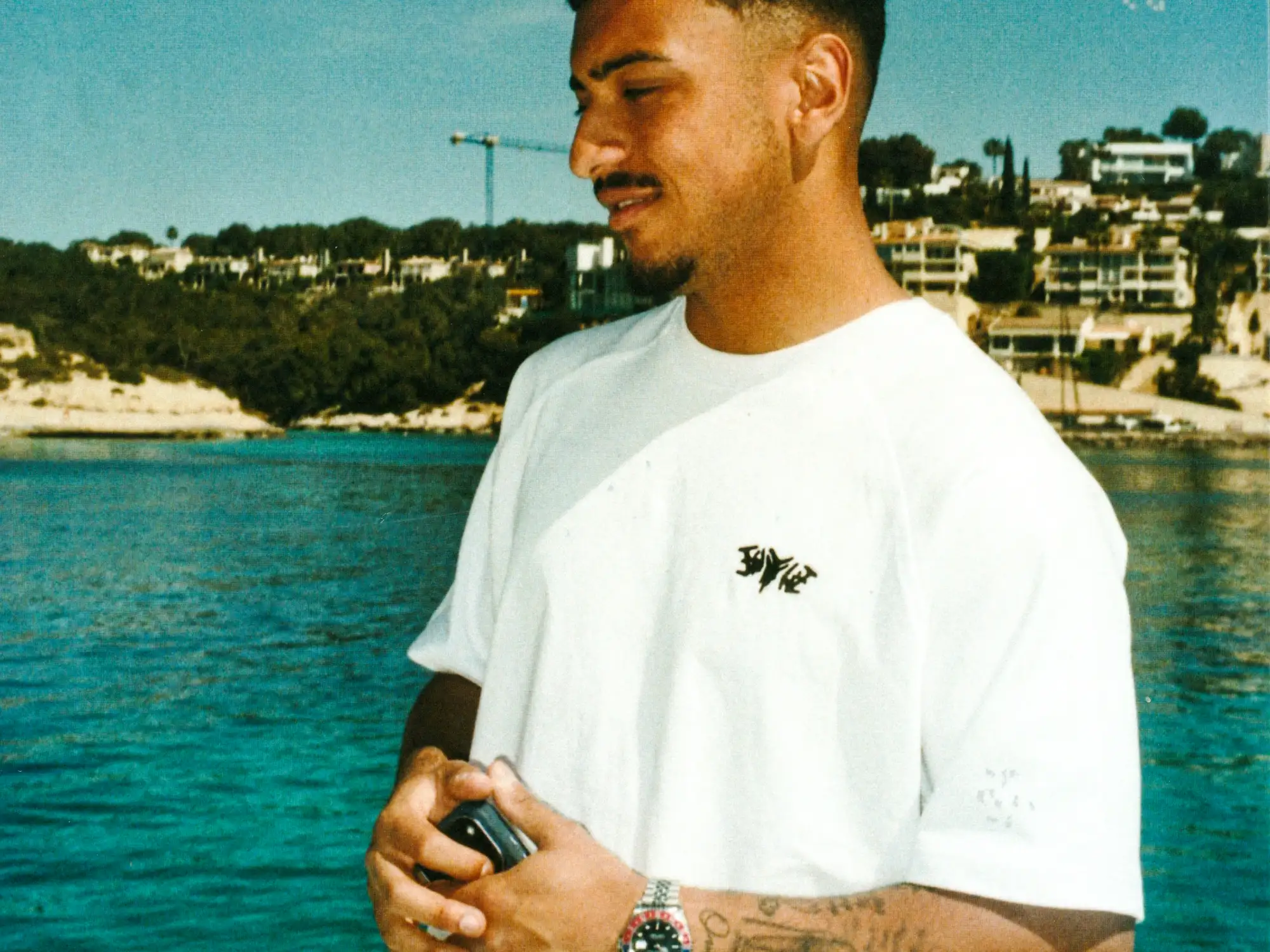 Keyshawn von 45Keys im weißen T-Shirt auf dem Yachtdeck vor dem türkisblauen Meer und Mallorcas Küste.