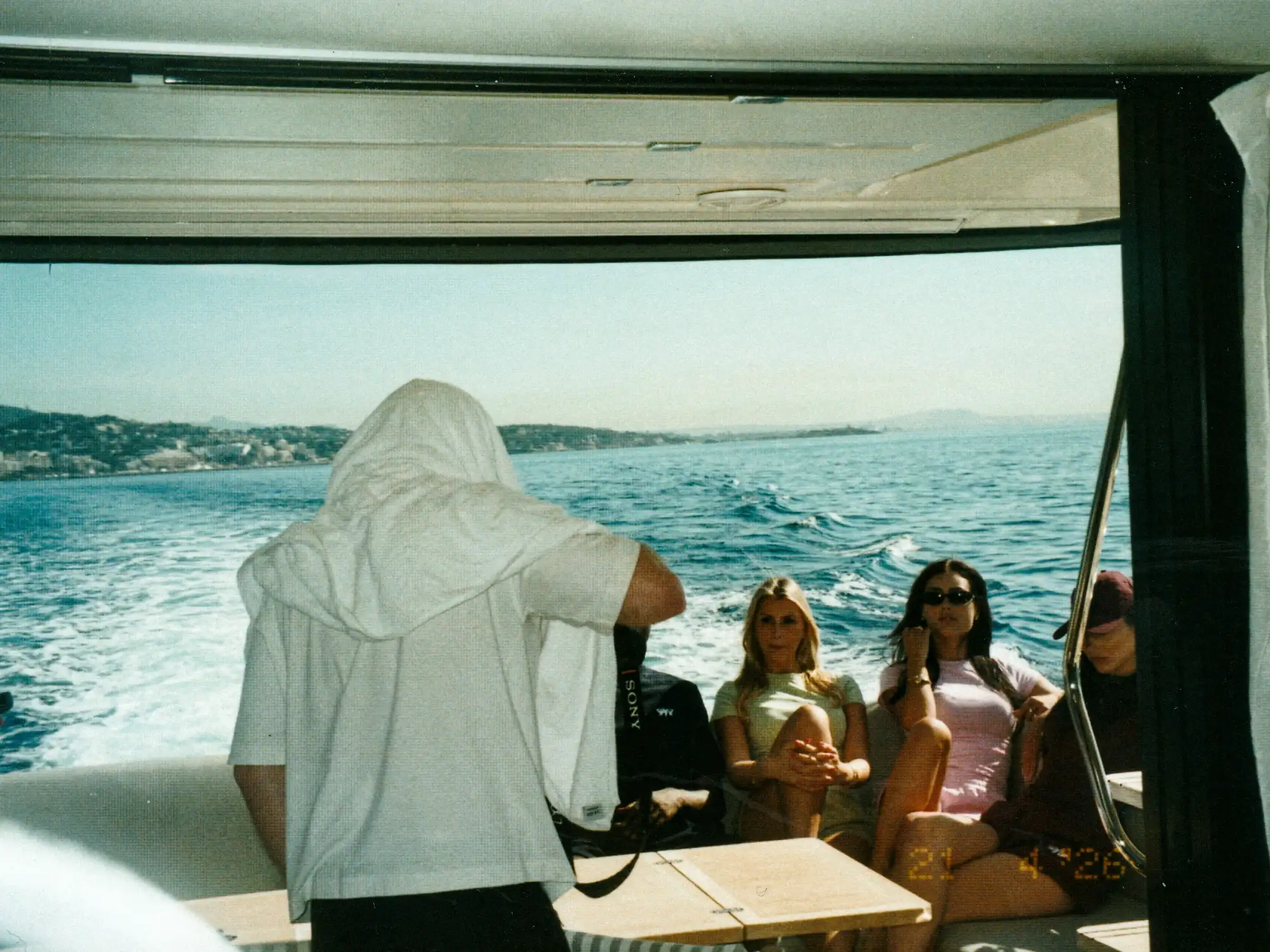 Alexander Gorszczynski mit weißer Kappe steht am Heck der Yacht vor den sitzenden Models.