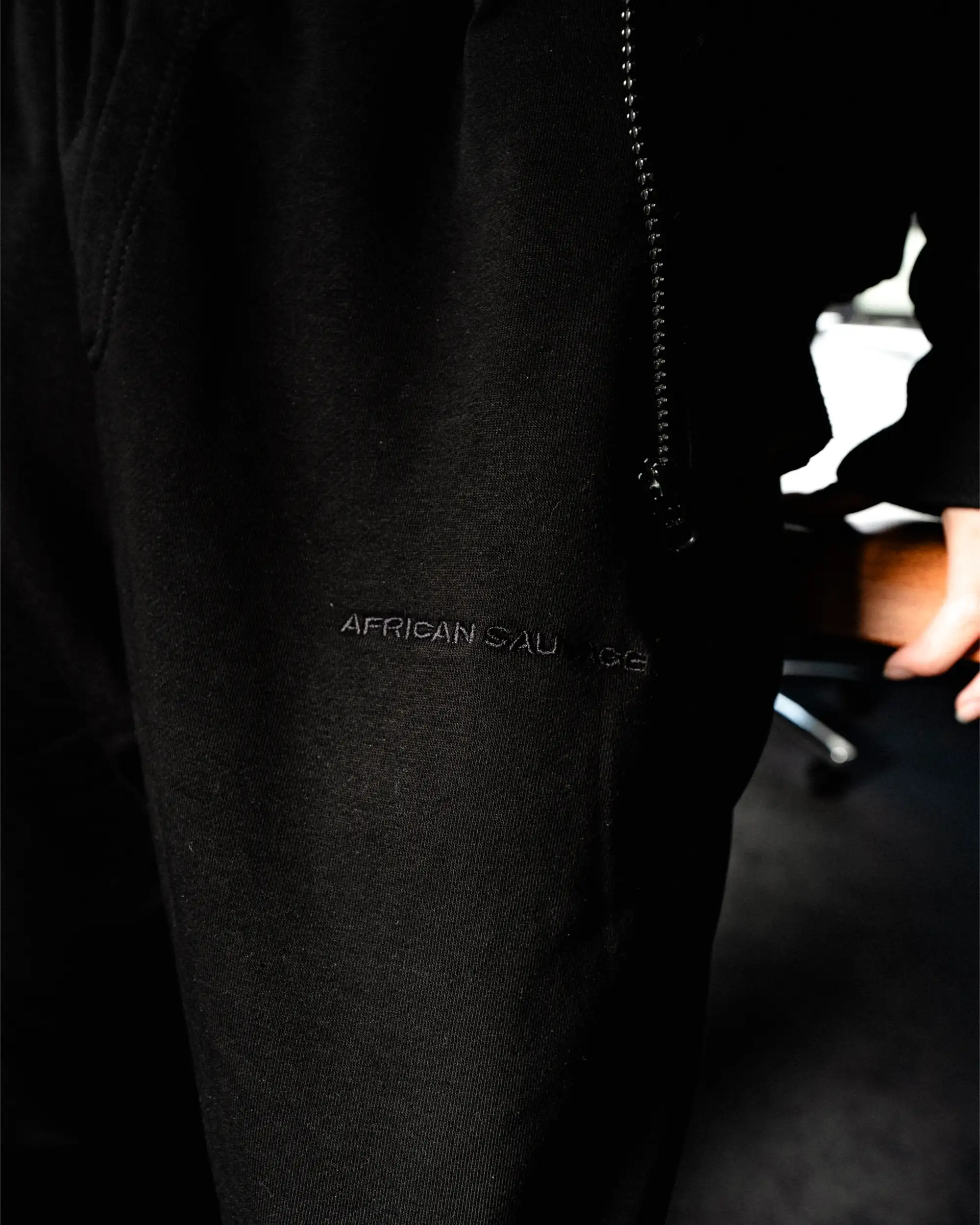 Detail der schwarzen Sweatpants von African Sauvage mit weißem Logo.