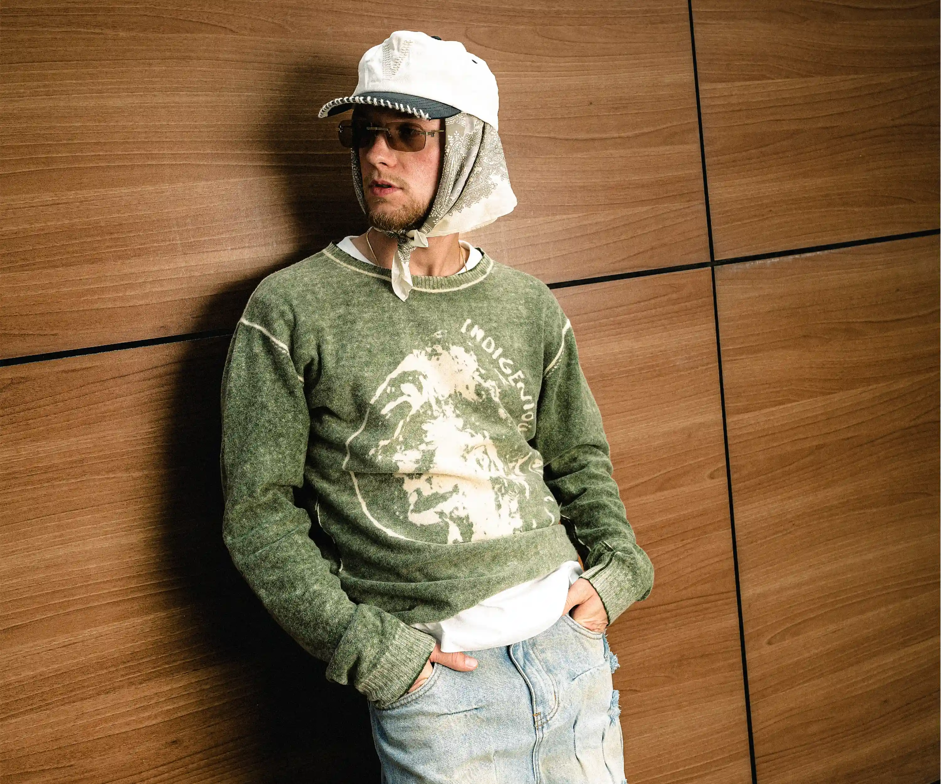 Strom mit Sonnenbrille, Kopftuch und grüner Jacke vor einer Holzwand beim Porträtshooting in Düsseldorf.