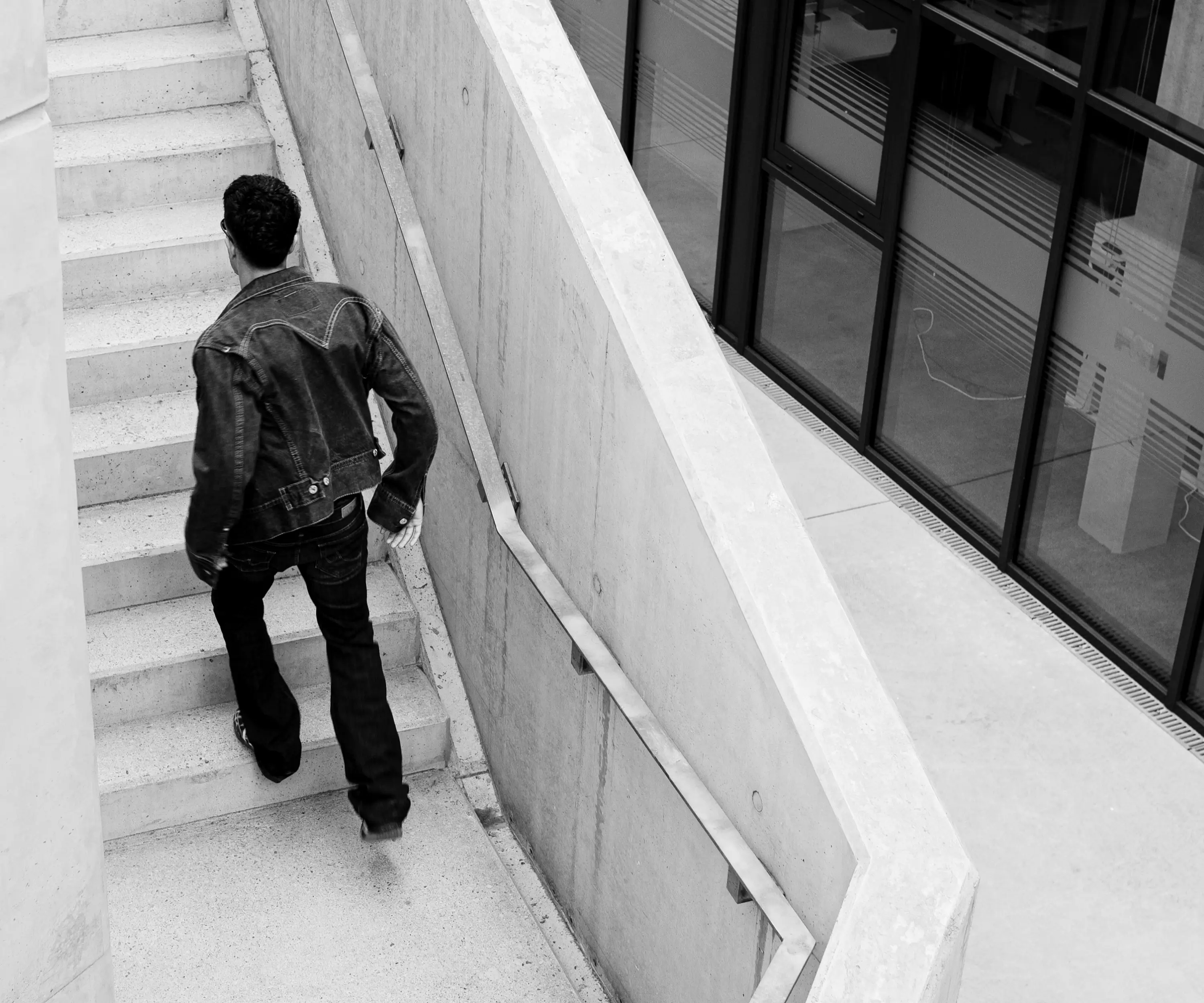 Schwarz-Weiß-Aufnahme von Ahmad im Denim-Look von hinten auf einer Treppe neben einer geschwungenen Wand.
