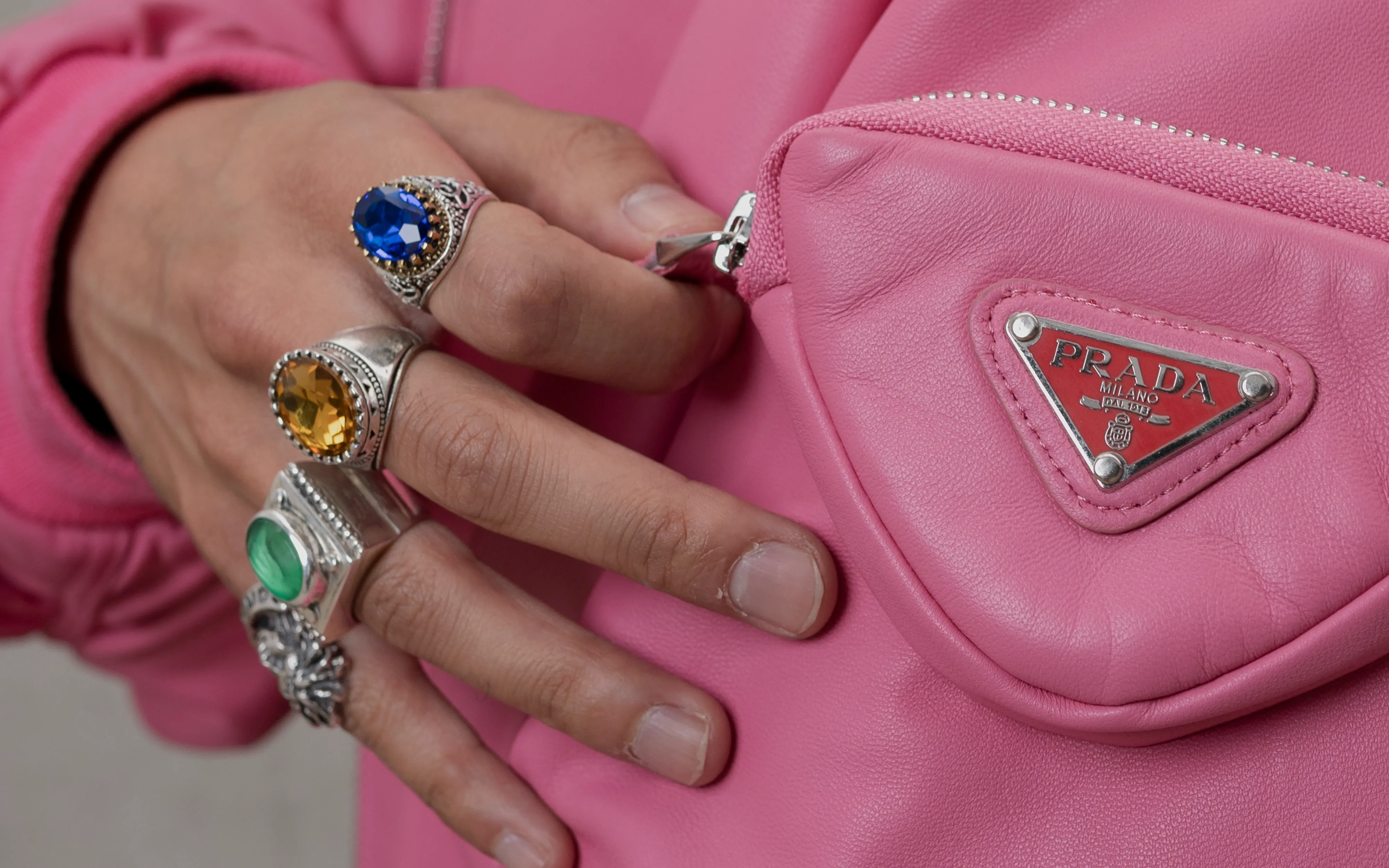 Detail von Ahmads Händen mit auffälligen Ringen vor der Tasche seiner pinken Prada-Bomberjacke.