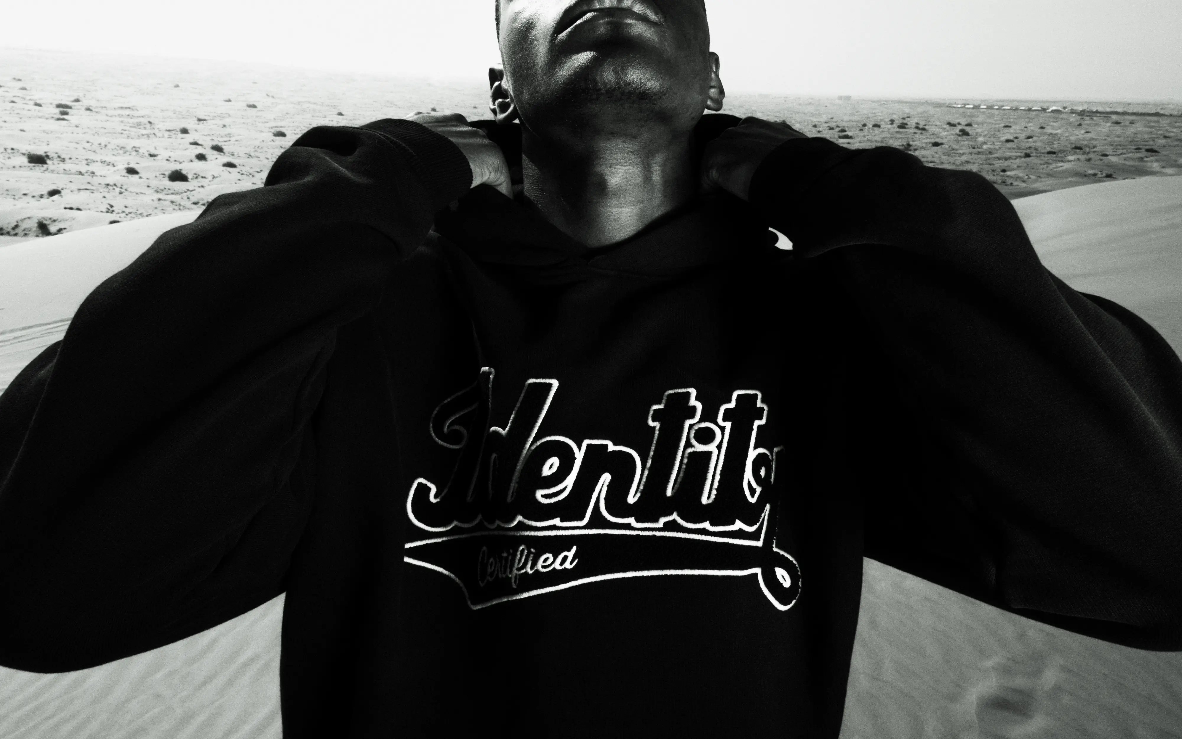 Schwarz-Weiß-Porträt von Ibo Ouro-Bodi im schwarzen Certified-Identity-Hoodie mit angehobenen Armen.