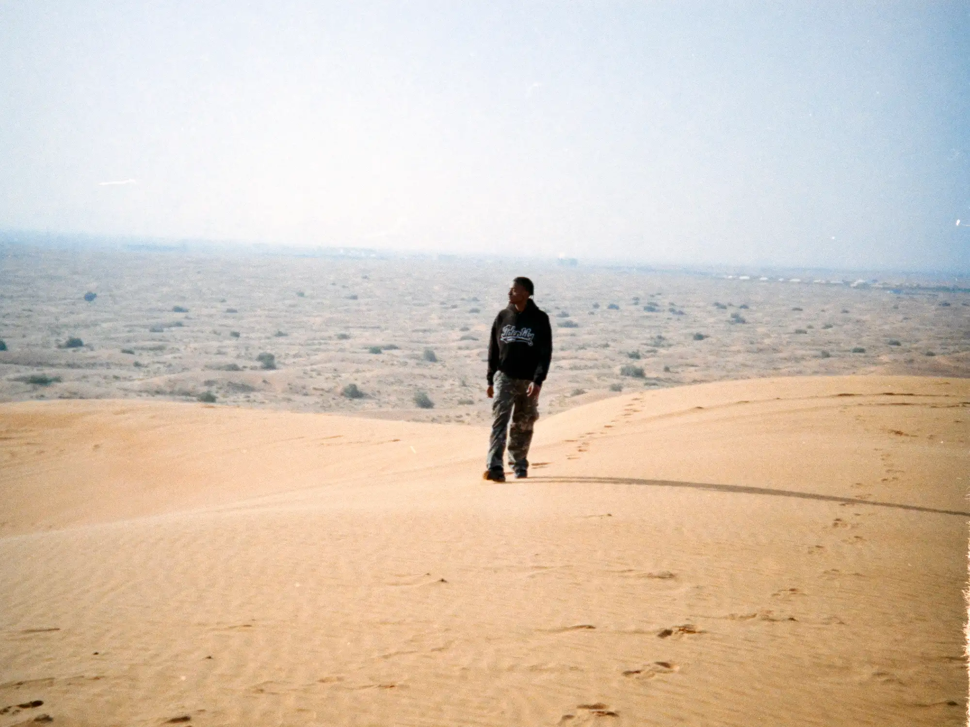 Analoge Aufnahme von Ibo Ouro-Bodi auf einer Sanddüne vor der weiten Wüstenlandschaft.
