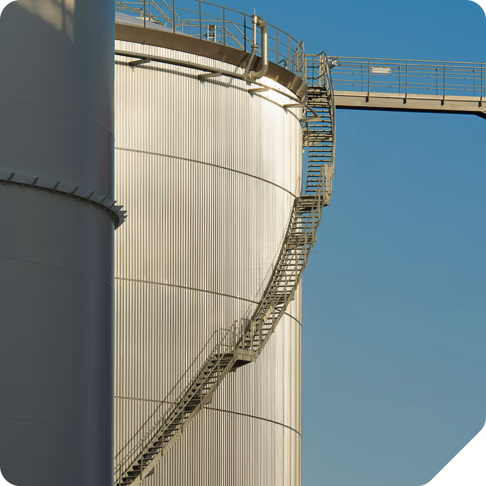 Metal industrial storage tanks under clear blue sky with a curved staircase attached to one tank.