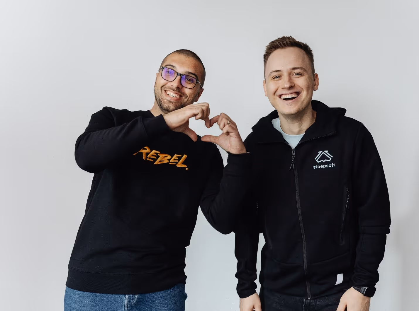 Two men making a heart with their handsDescription automatically generated
