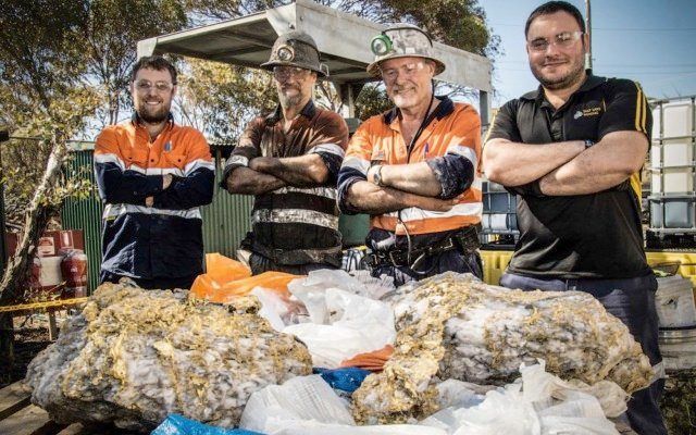 A group of four mining workers stand proudly in front of a huge hunk of gold ore.