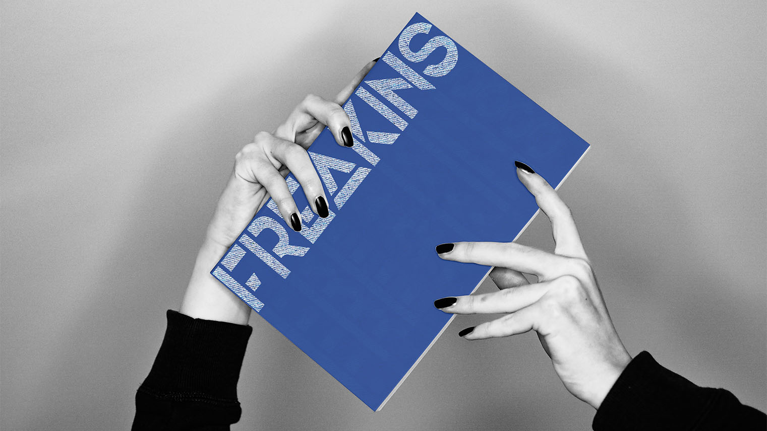 Two hands with black nail polish holding a blue Brand book titled FRAKINS against a gray background.