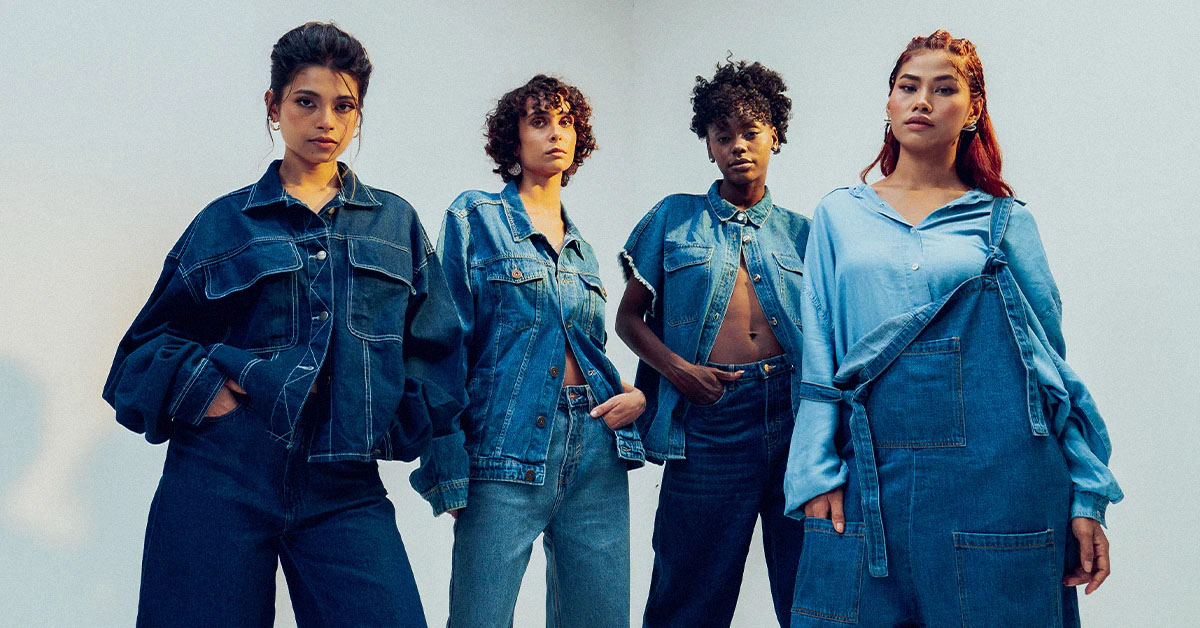 Four diverse women standing in a row, modeling various styles of blue denim clothing against a plain background.