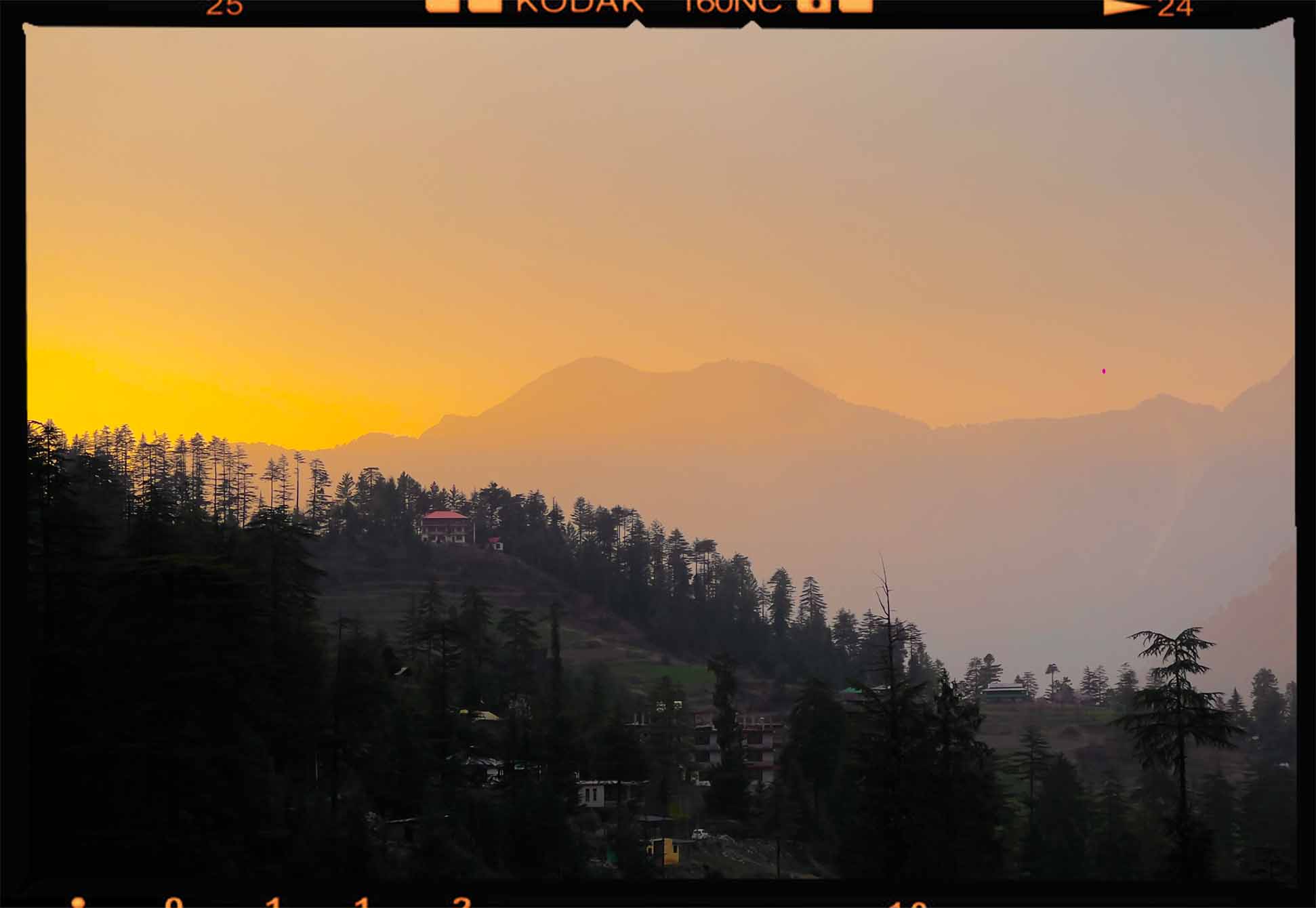 Sunset over a mountainous forested landscape with scattered houses on hills.