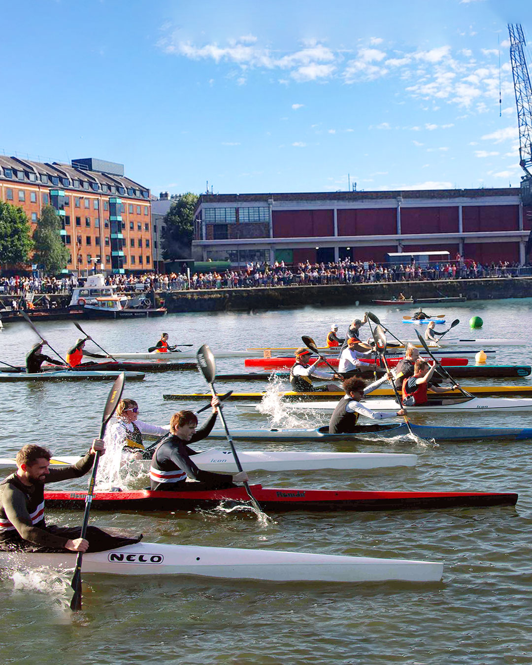 A group of canoeists paddle at speed through Bristol’s Harbourside during a competitive race, each wearing life jackets and concentrating intensely. The Bristol Canoe Club logo is prominently overlaid at the top, featuring paddles and the Clifton Suspension Bridge with the words “Canoe – SUP – Kayak.” Historic buildings and moored boats line the waterfront in the background.