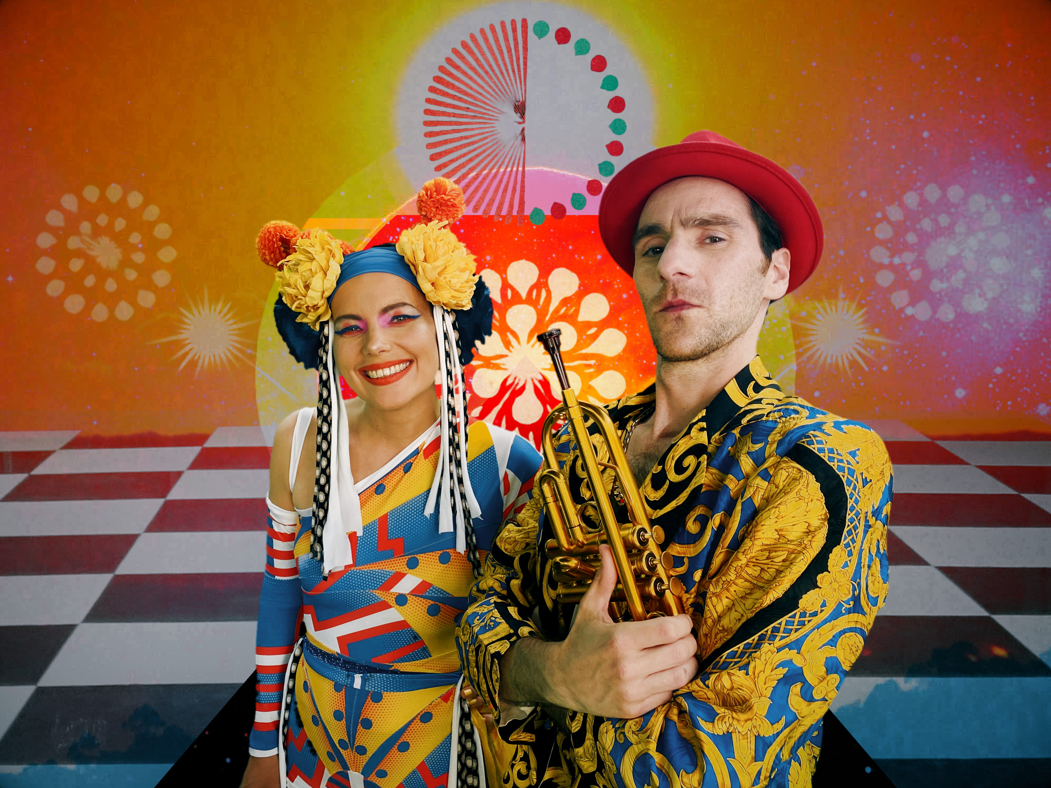 Two colourful performers pose against a vibrant, retro-style backdrop with bold patterns and a checkerboard floor, one smiling and the other holding a trumpet.