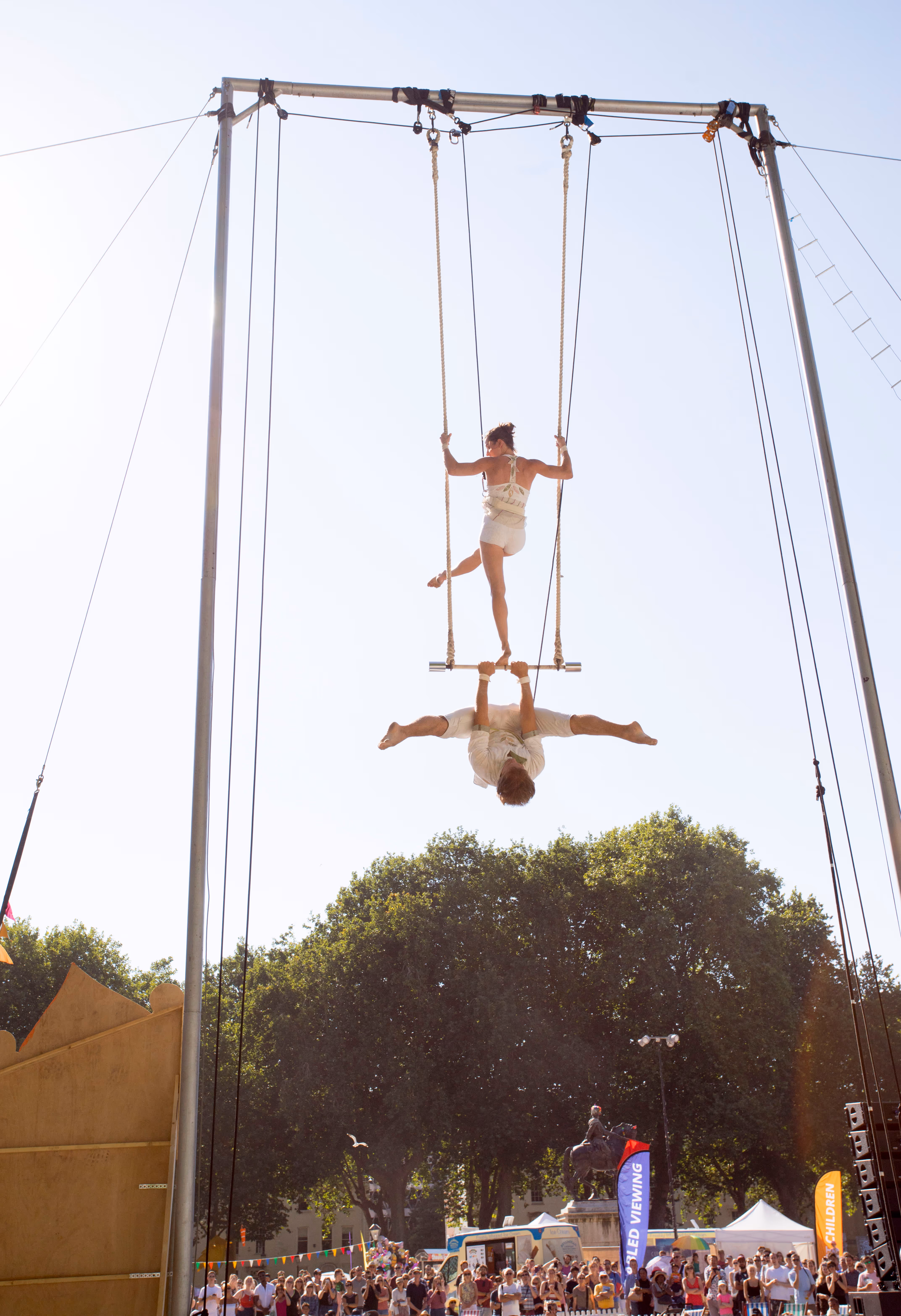 2 circus performers hanging on apparatus 