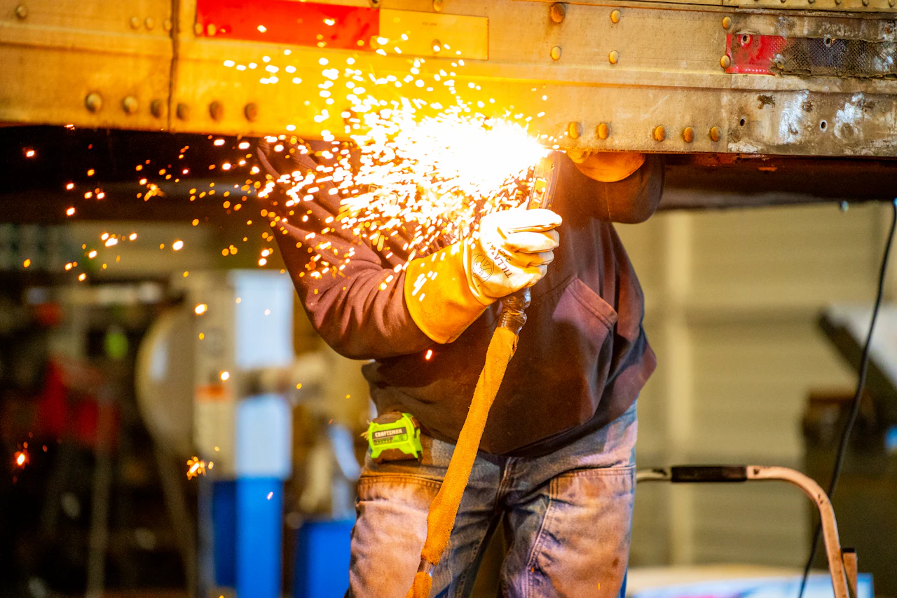 mechanic welding a truck frame in a shop bay 