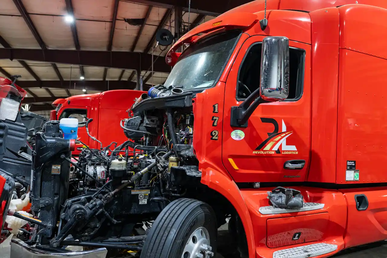 Heavy-duty truck repair on red Revolution Logistics semi 172 with hood removed, exposing engine, hoses and wiring.