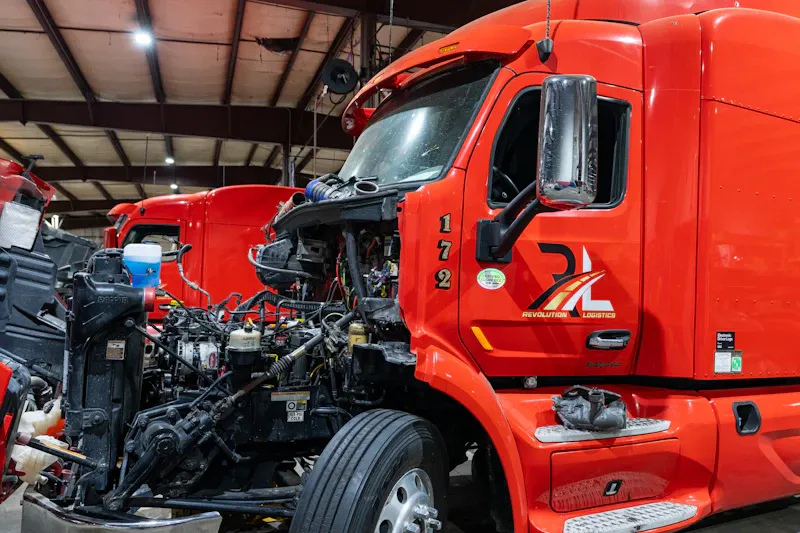 Heavy-duty truck repair on red Revolution Logistics semi 172 with hood removed, exposing engine, hoses and wiring.