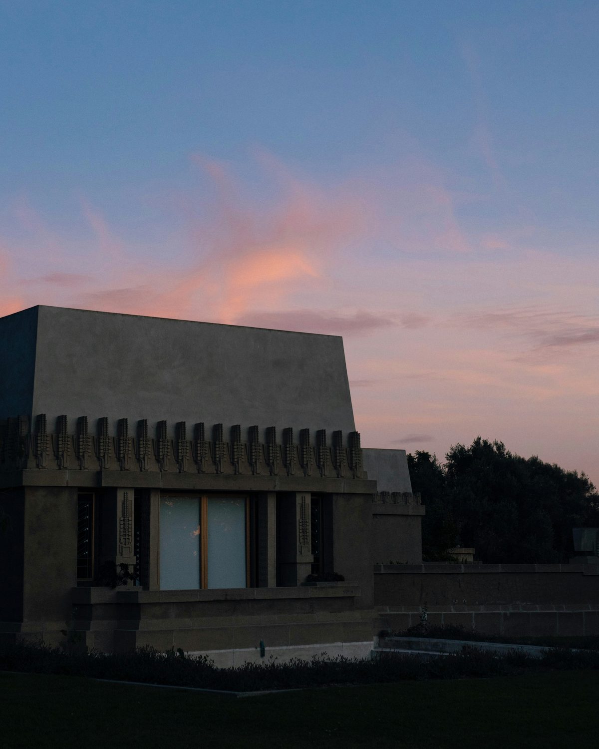 Hollyhock House in silhouette against a pink and orange sunset sky