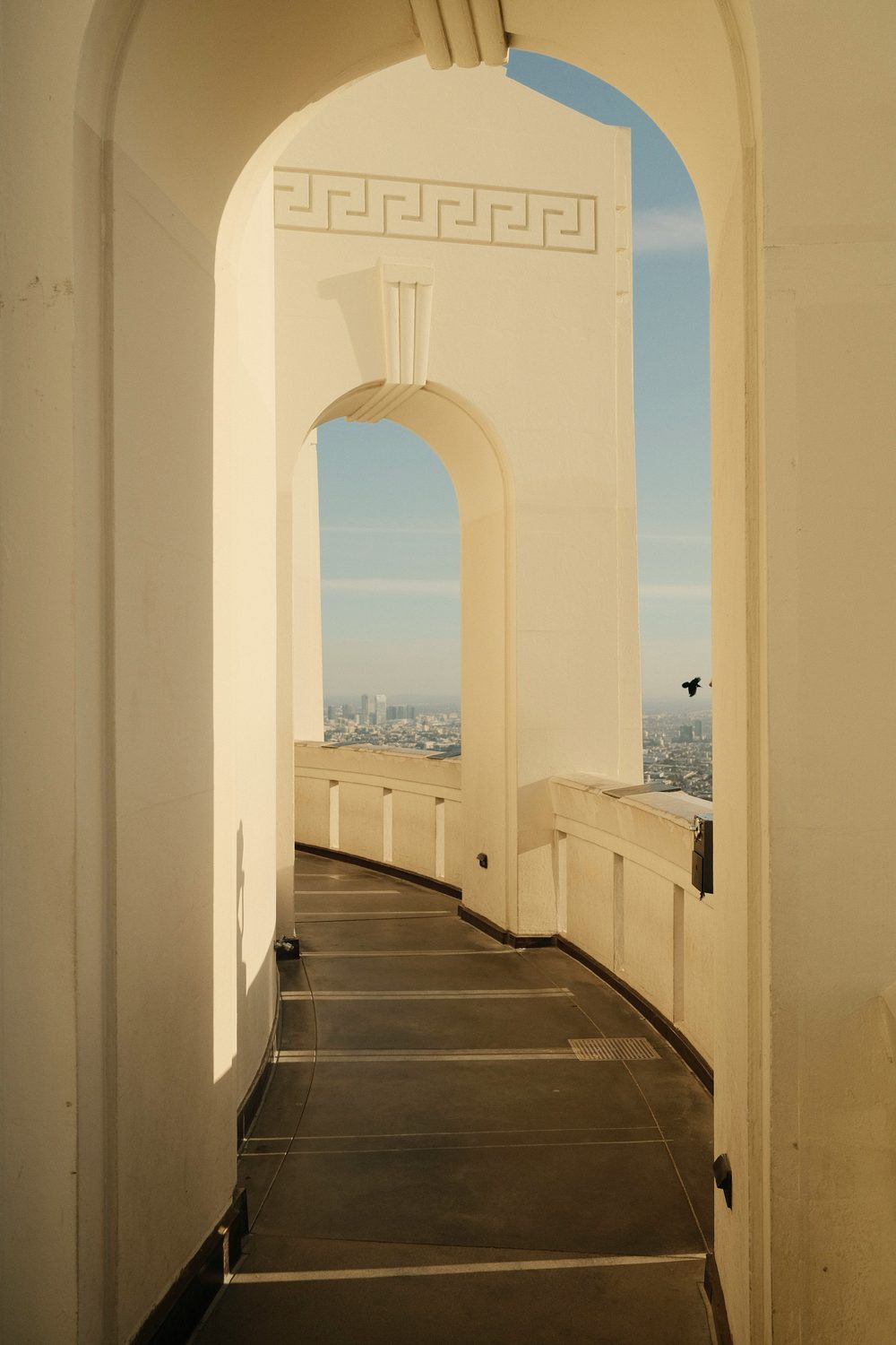 A curved, arched walkway at Griffith Observatory glowing at golden hour, with the city visible through the arches