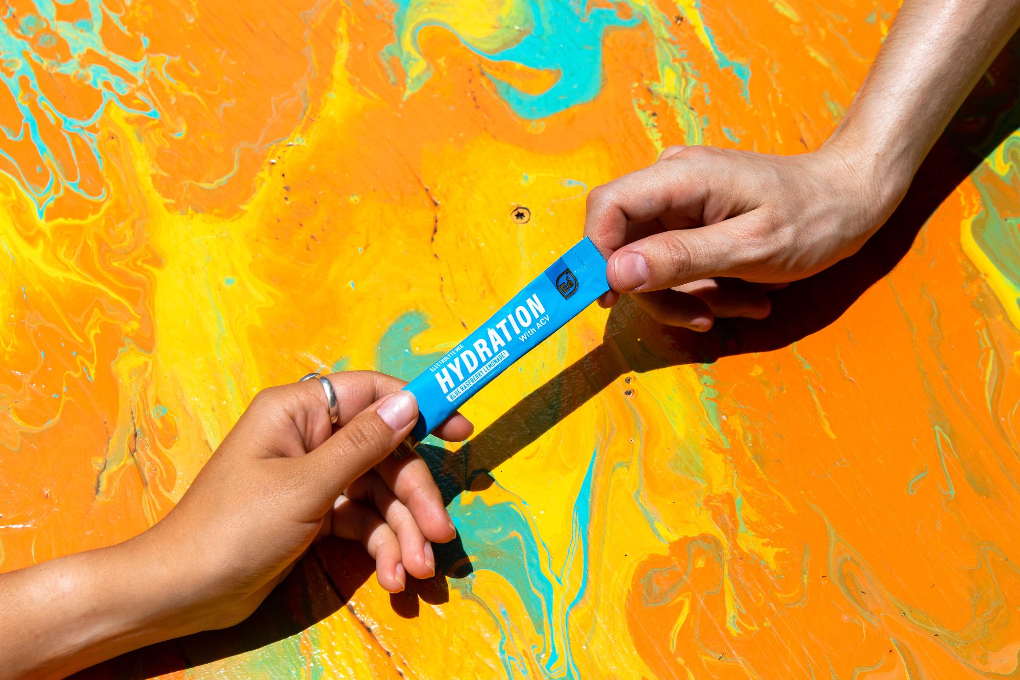 Two hands pass a hydration stick over an orange marbled background