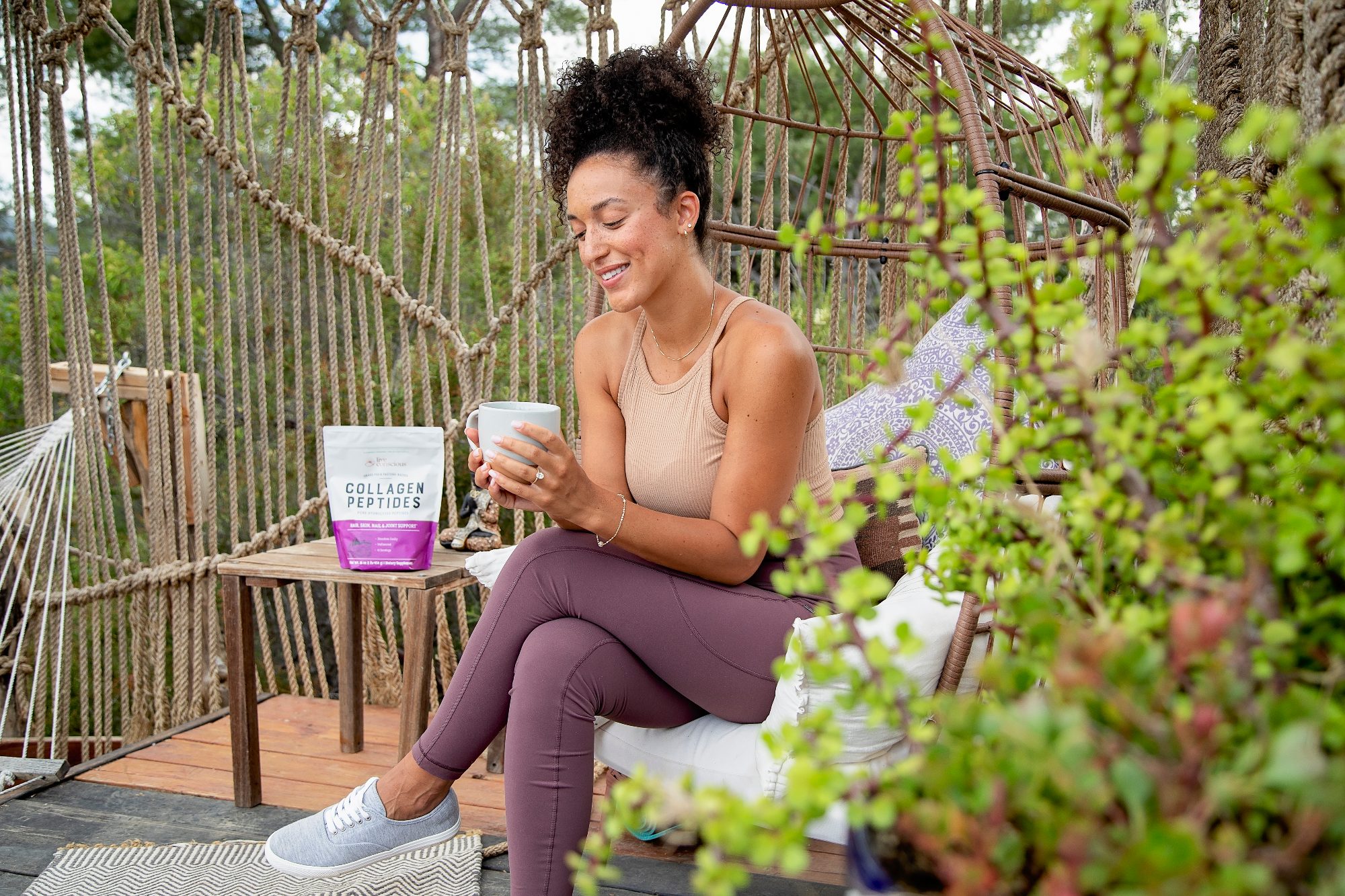 A woman sits in a garden holding a Live Conscious drink