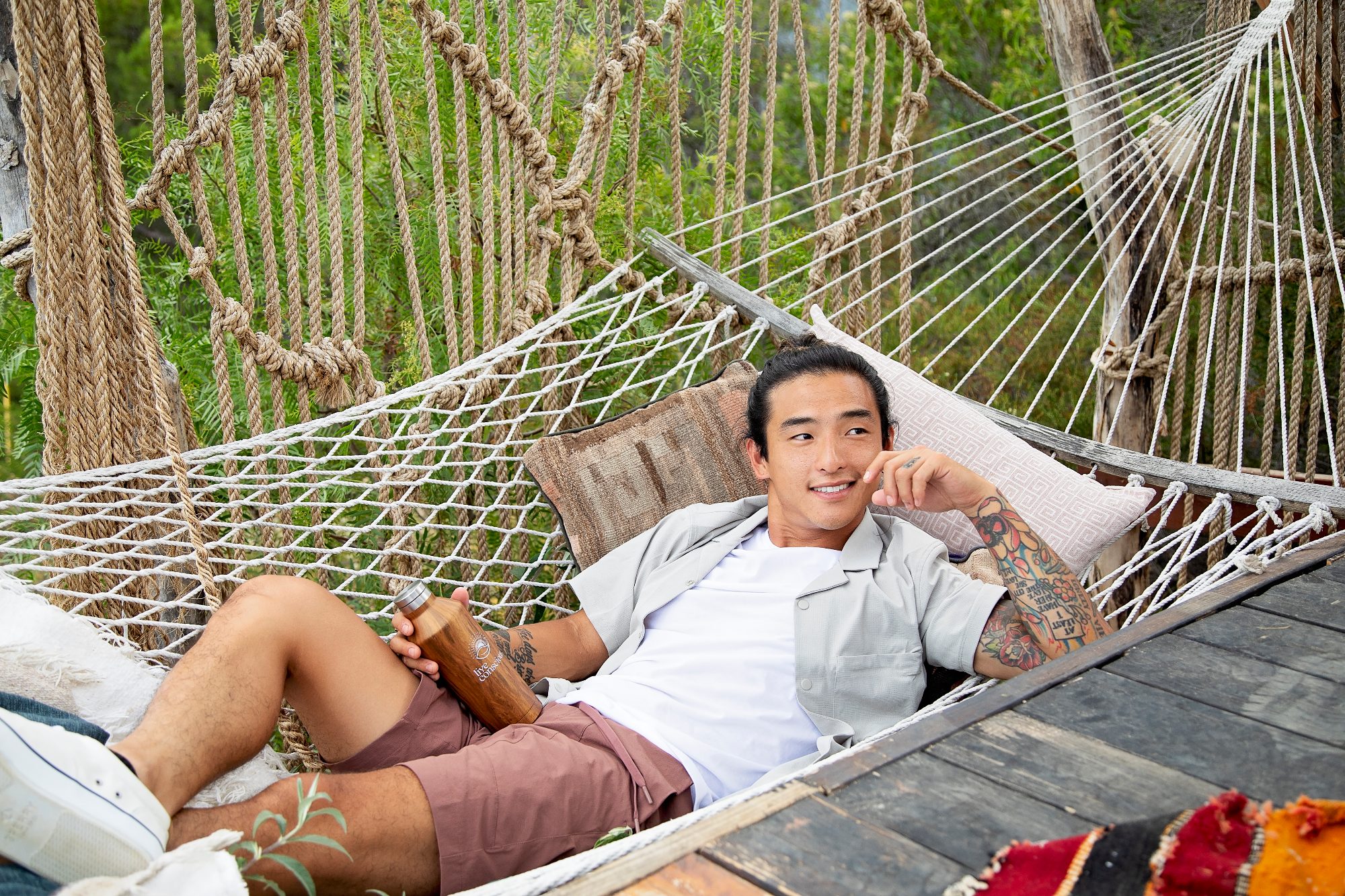 A man relaxes in a rope hammock with a drink