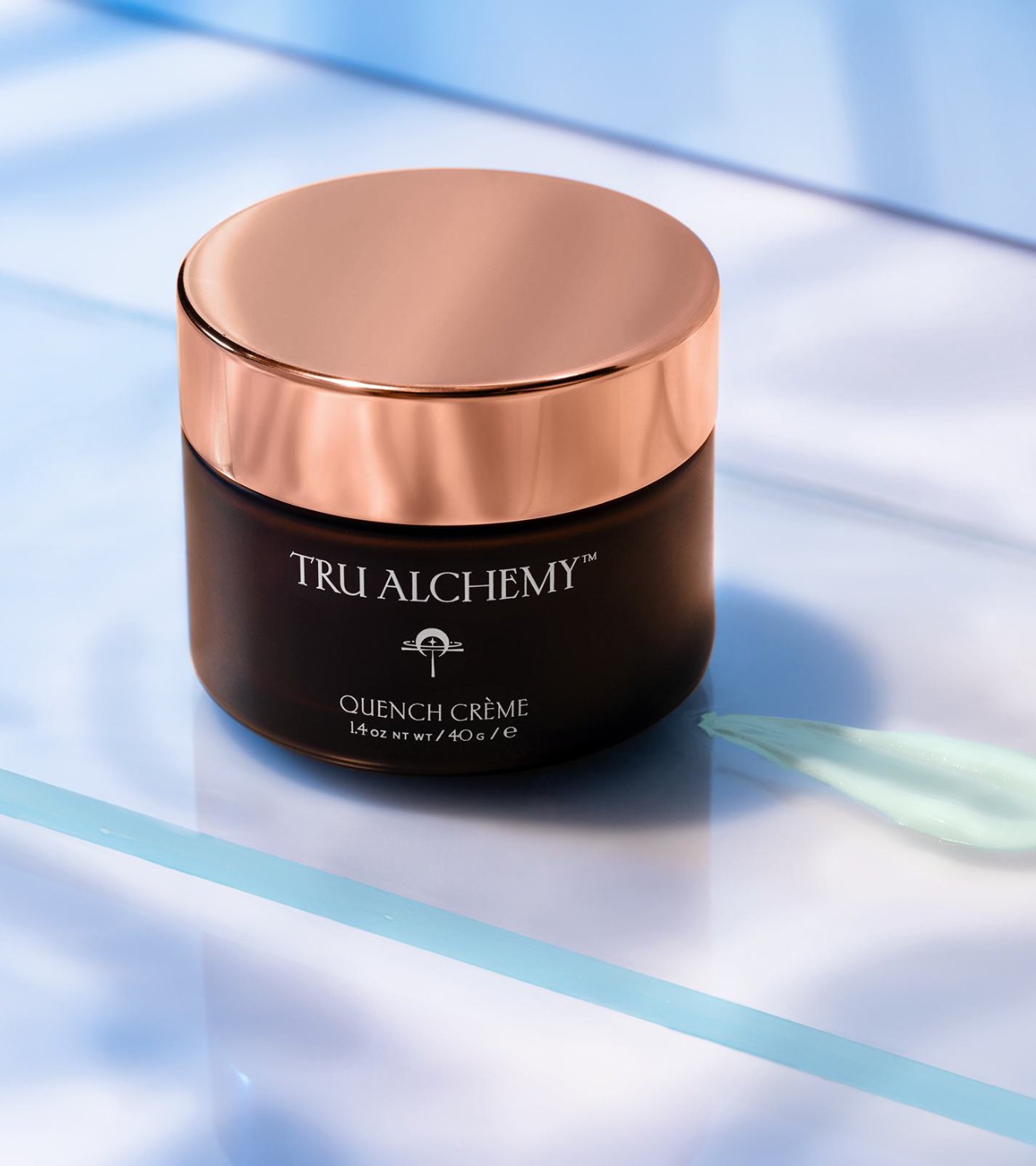 Tru Alchemy Quench Crème jar with a rose gold lid on blue glass