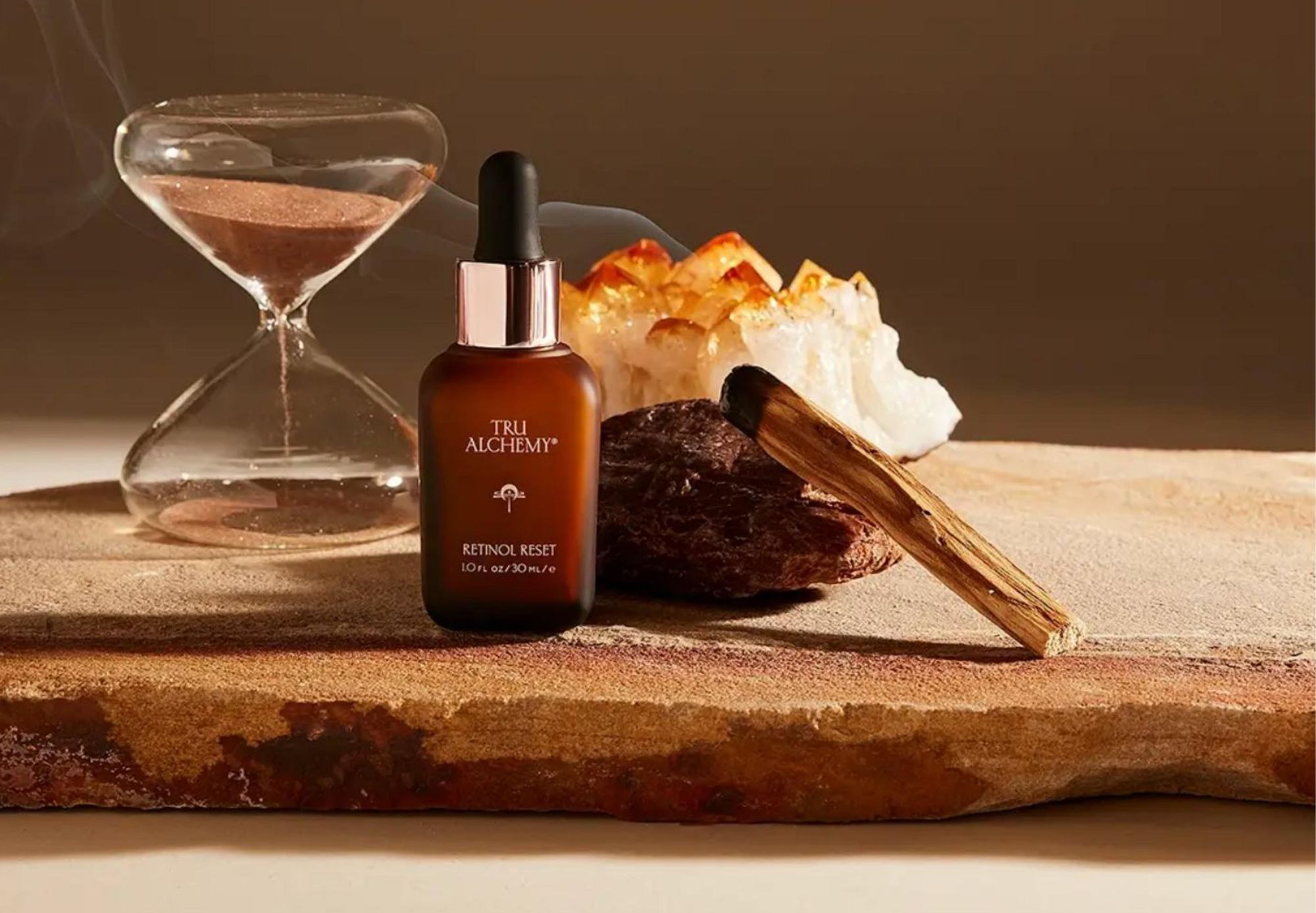 Tru Alchemy Retinol Reset bottle on a stone slab beside an hourglass, crystals and palo santo