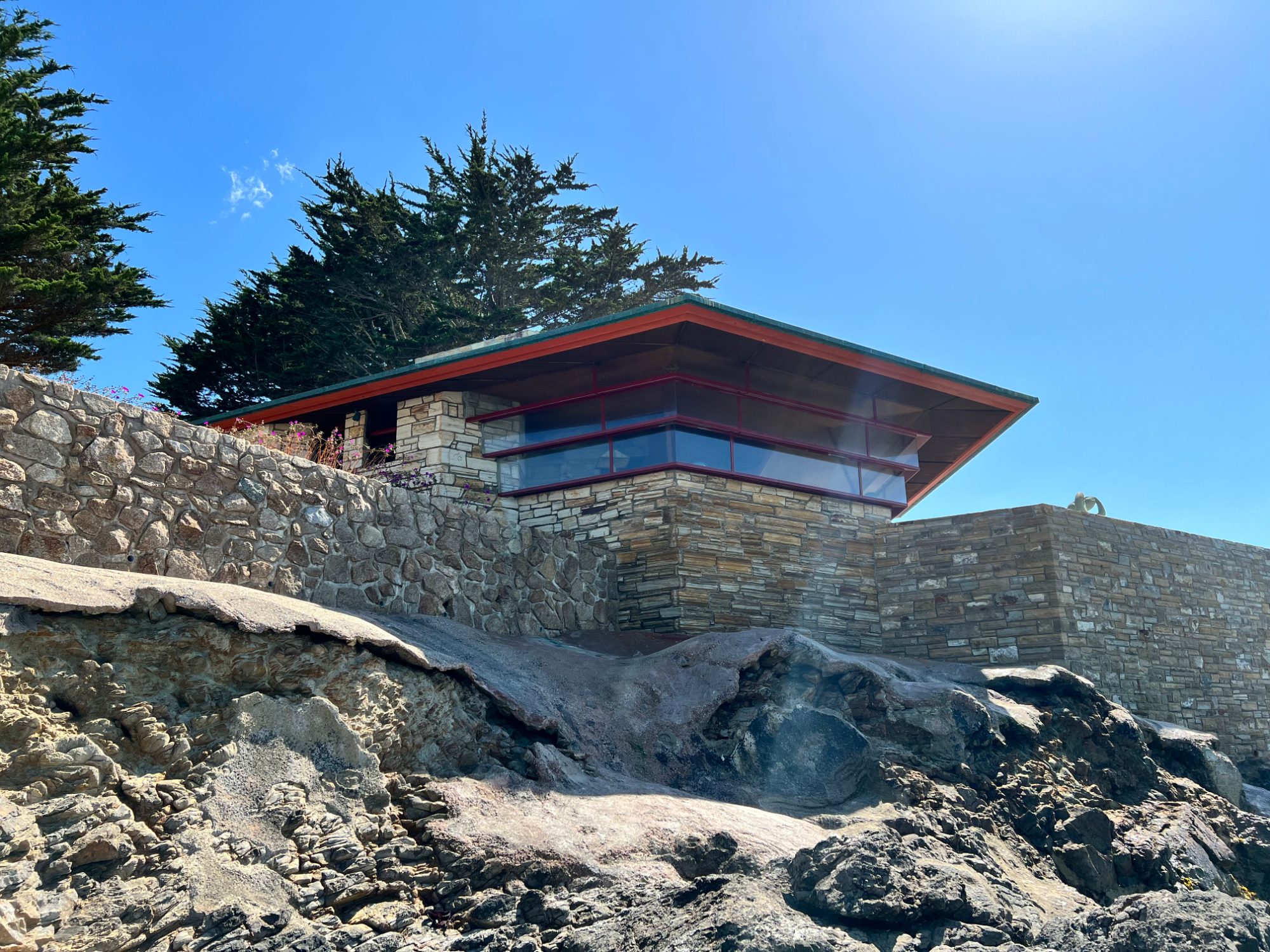 Frank Lloyd Wright's Mrs. Clinton Walker House on Carmel Point, a low house with an overhanging roof above a stone base on the rocks