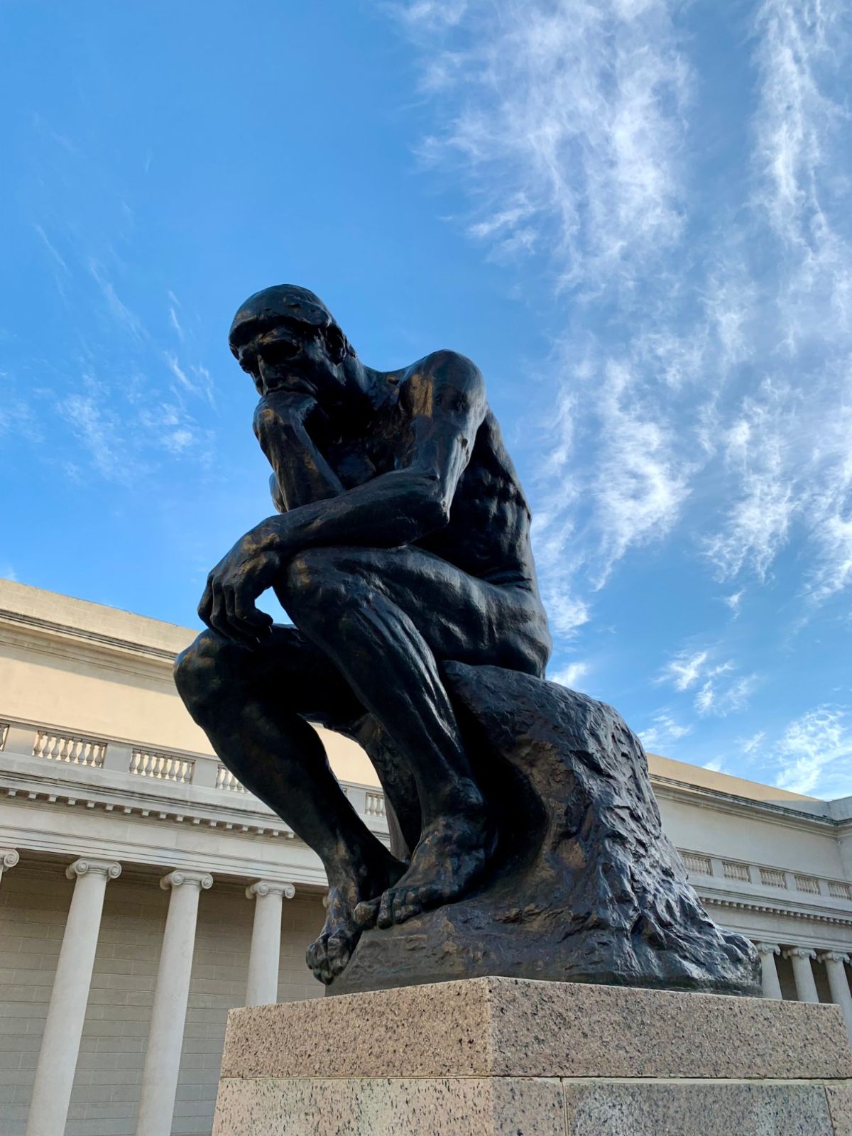 Rodin's bronze Thinker seated on a granite base in the Court of Honor, with the columns of the Legion of Honor behind it and a blue sky above