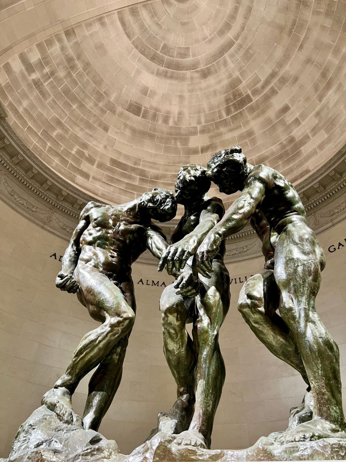Rodin's Three Shades, three bronze figures leaning together with their heads bowed, under a domed ceiling inside the Legion of Honor