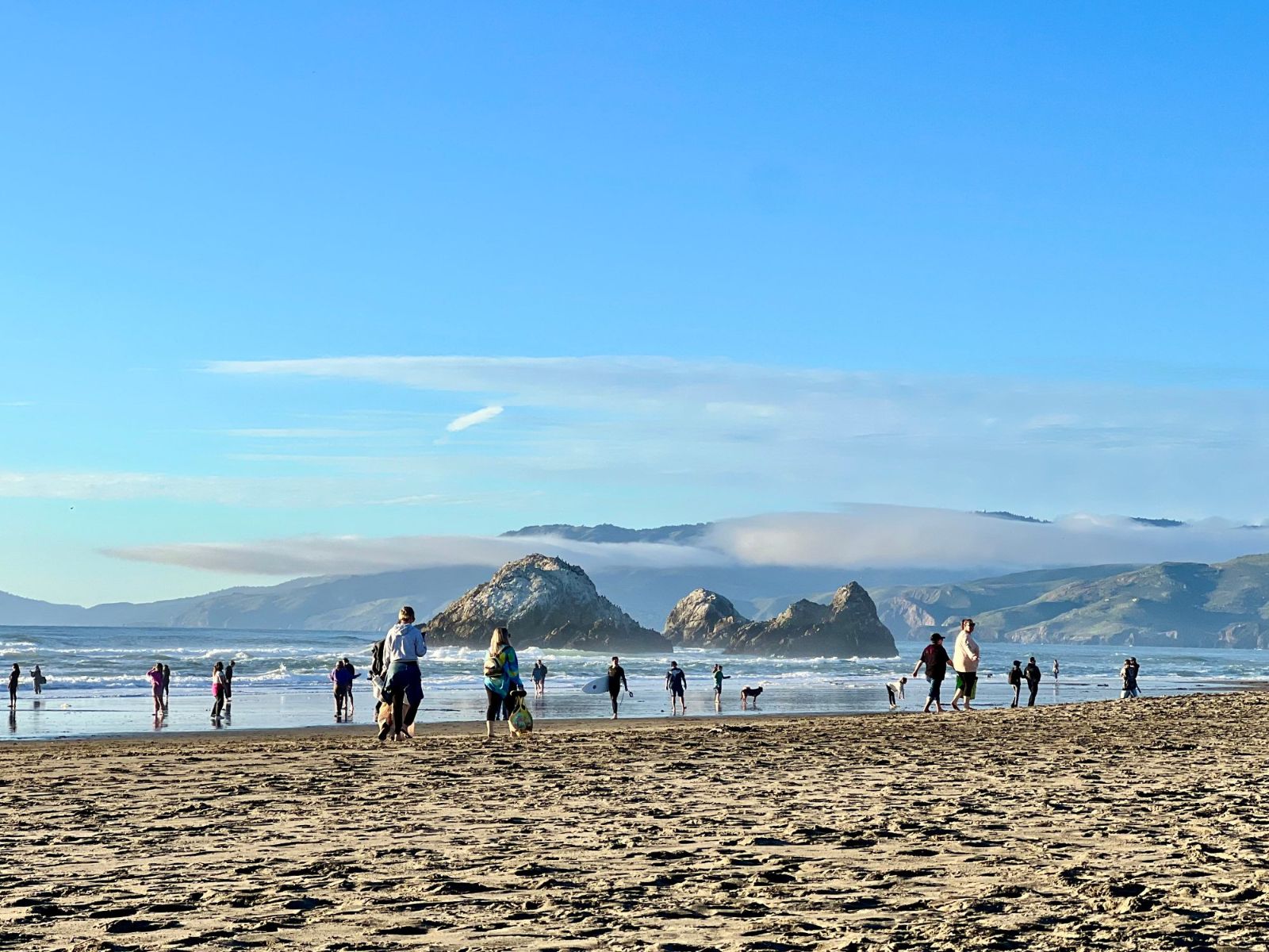 Walkers on Ocean Beach looking north toward offshore rocks, with a bank of fog behind them
