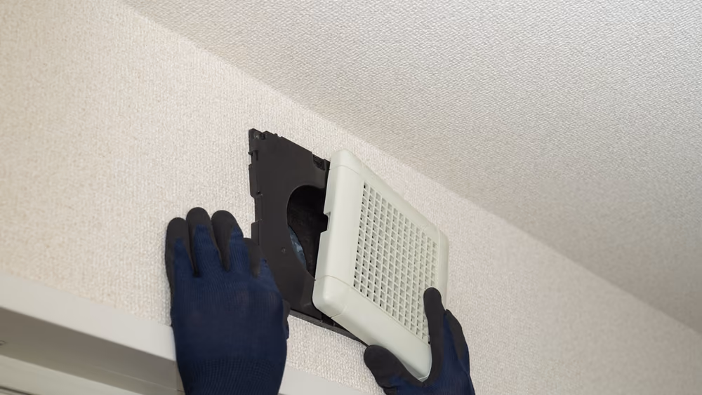 A professional technician wearing a safety mask carefully inspecting and cleaning a commercial ceiling air duct to improve HVAC system efficiency in Mt. Shasta