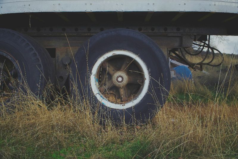 Dual semi-trailer wheels partially hidden by tall grass, highlighting weathered tires and metal undercarriage in rural outdoor setting.