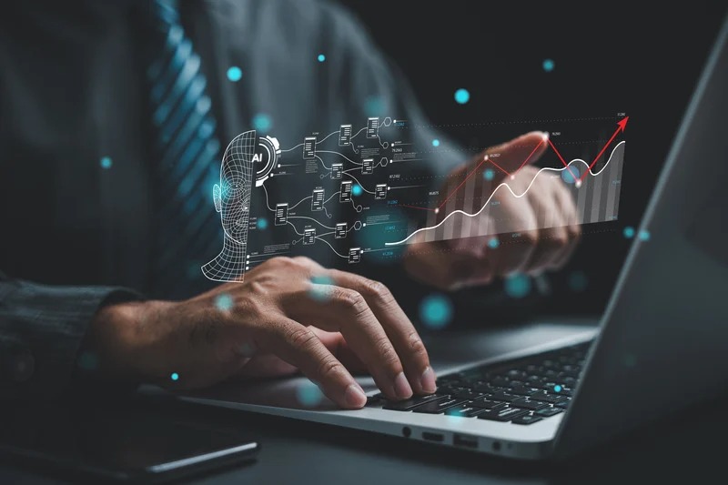 A man typing on a laptop with a floating digital graphic of an AI face model, a structured data map, and an upward-trending growth chart.