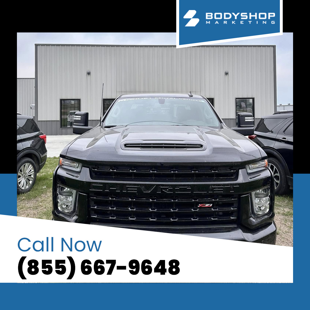 Front view of a black Chevrolet Silverado truck parked outside a modern commercial auto body facility.