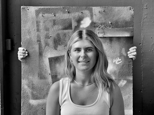 Smiling woman with shoulder-length hair stands in front of a textured board held up by two hands on either side.