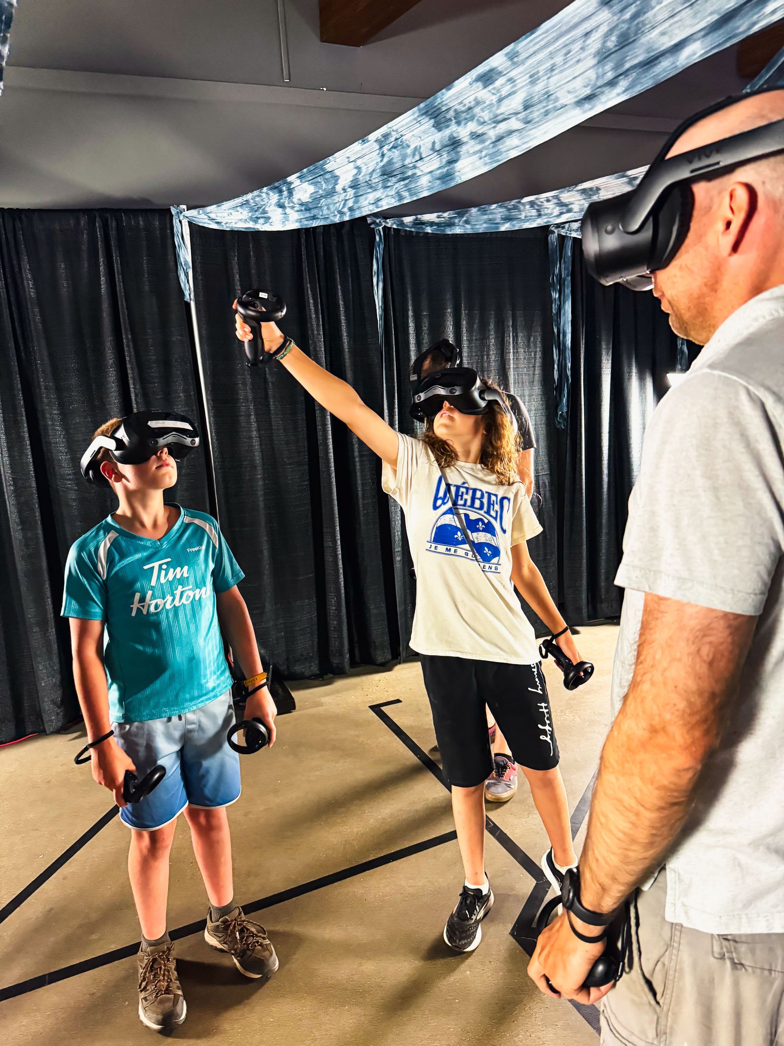Two young guests reaching into the virtual environment while an Adventure Portal operator guides the session