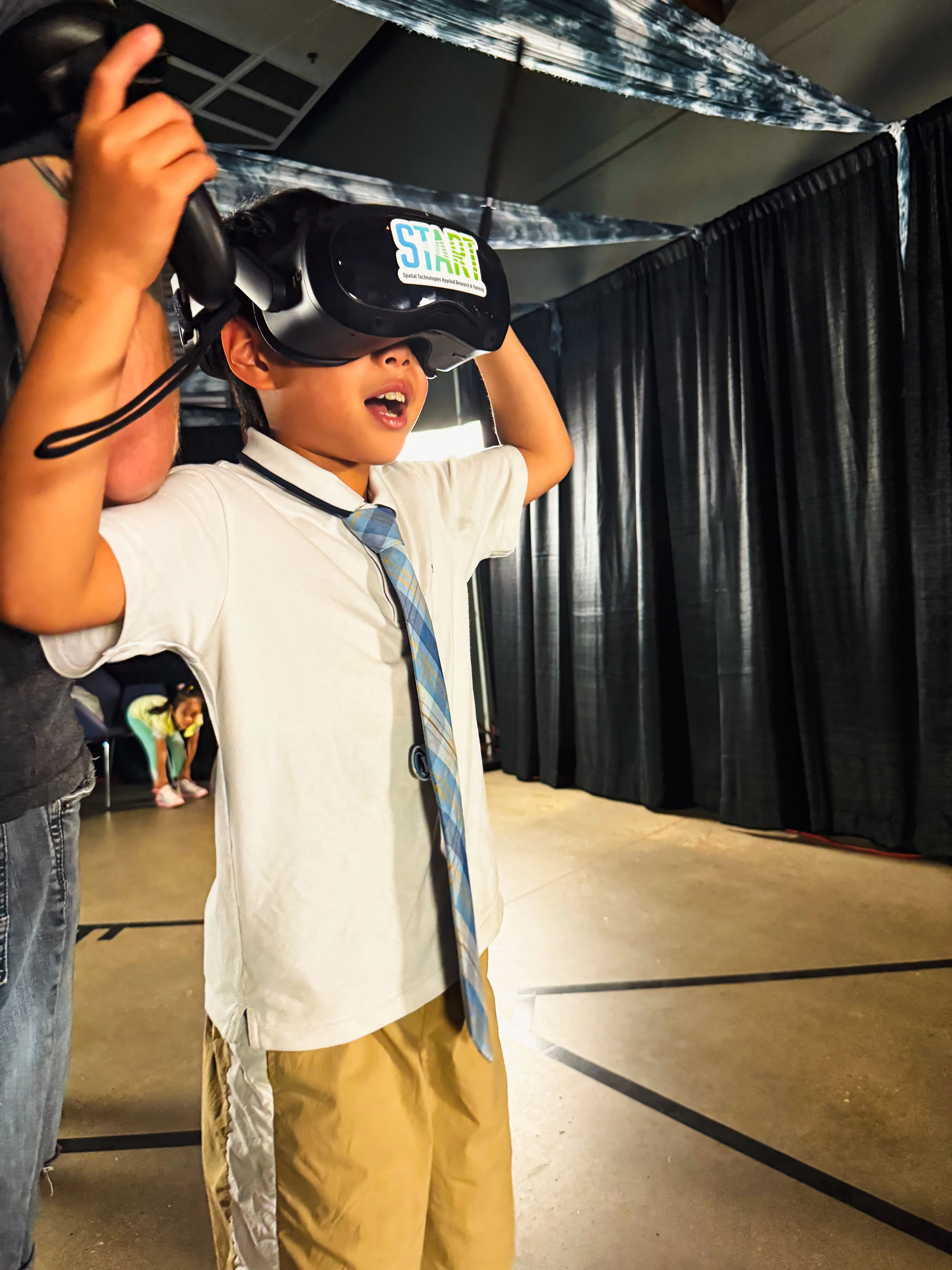 A staff member helps a student pull on a VR headset marked with a start sticker.