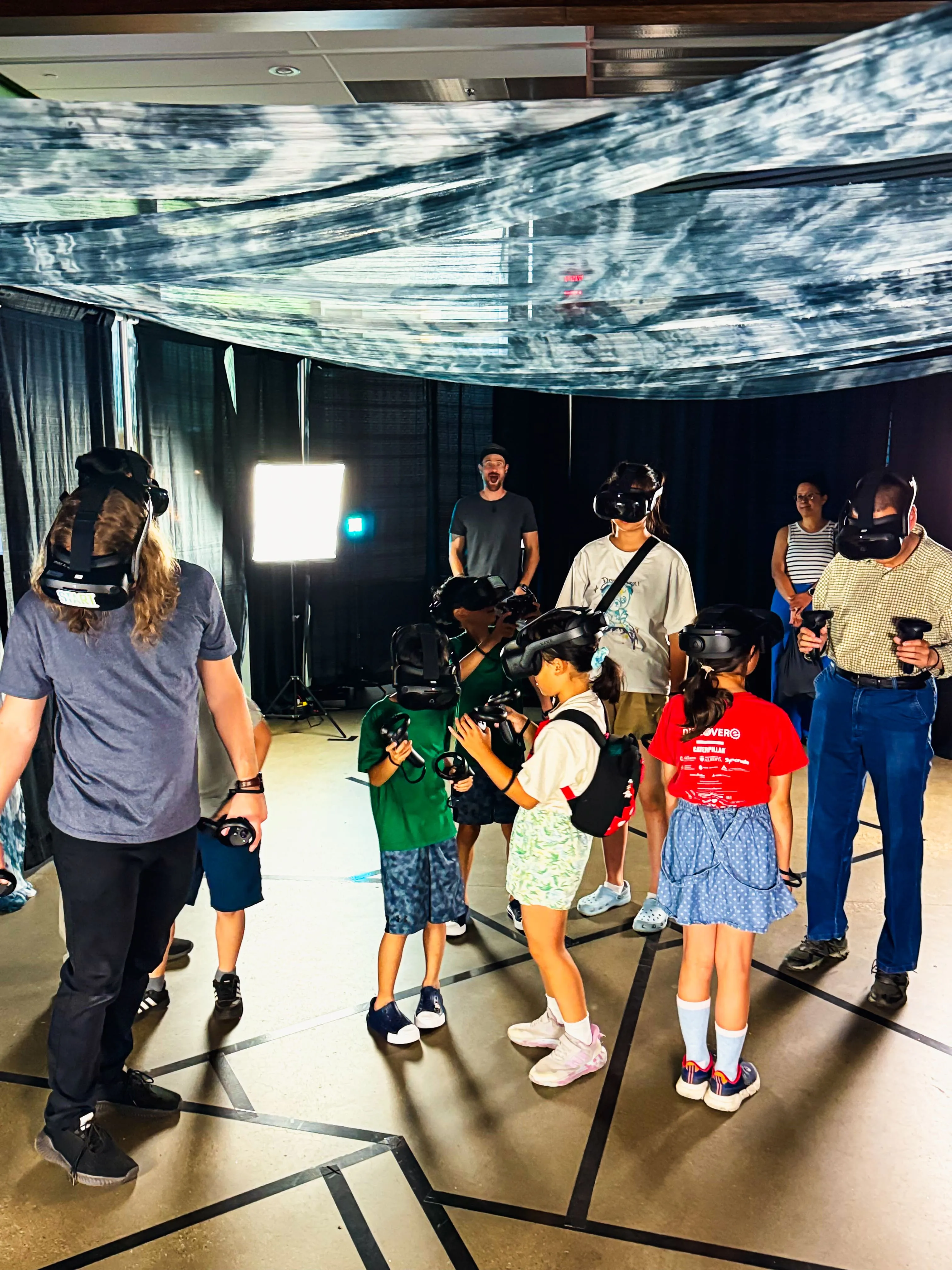 An Adventure Portal operator watches over a group of children and adults in VR headsets inside the arena.