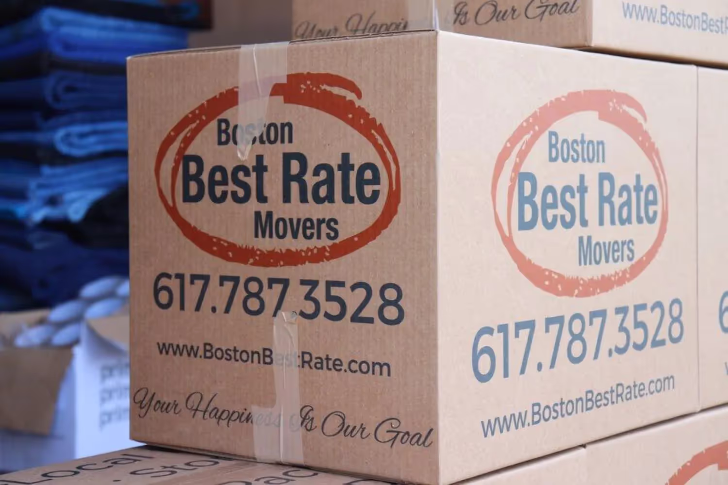 Two movers wearing Boston Best Rate Movers hoodies are loading a large wrapped item into a moving truck filled with boxes.