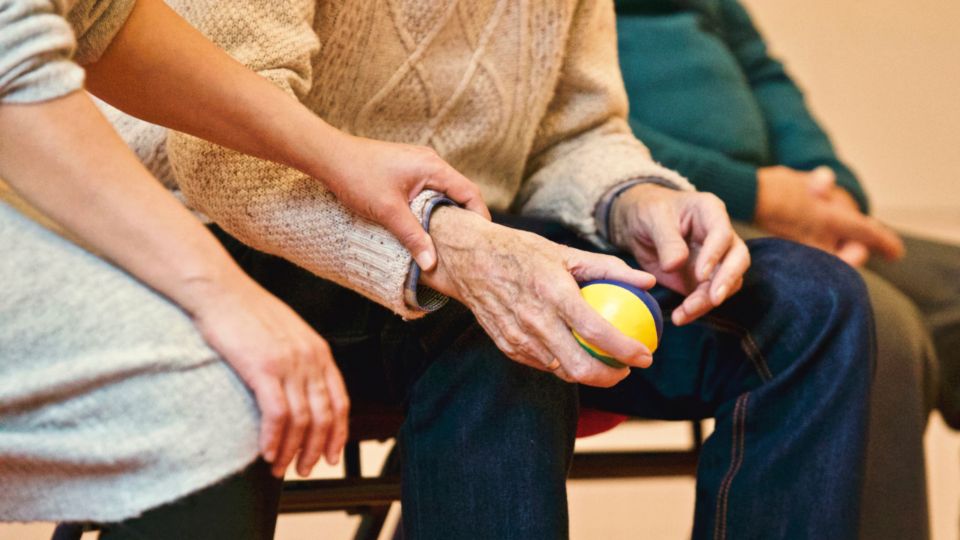Angehörige hält die Hand einer älteren pflegebedürftigen Person , die einen Stressball zur Beruhigung nutzt.