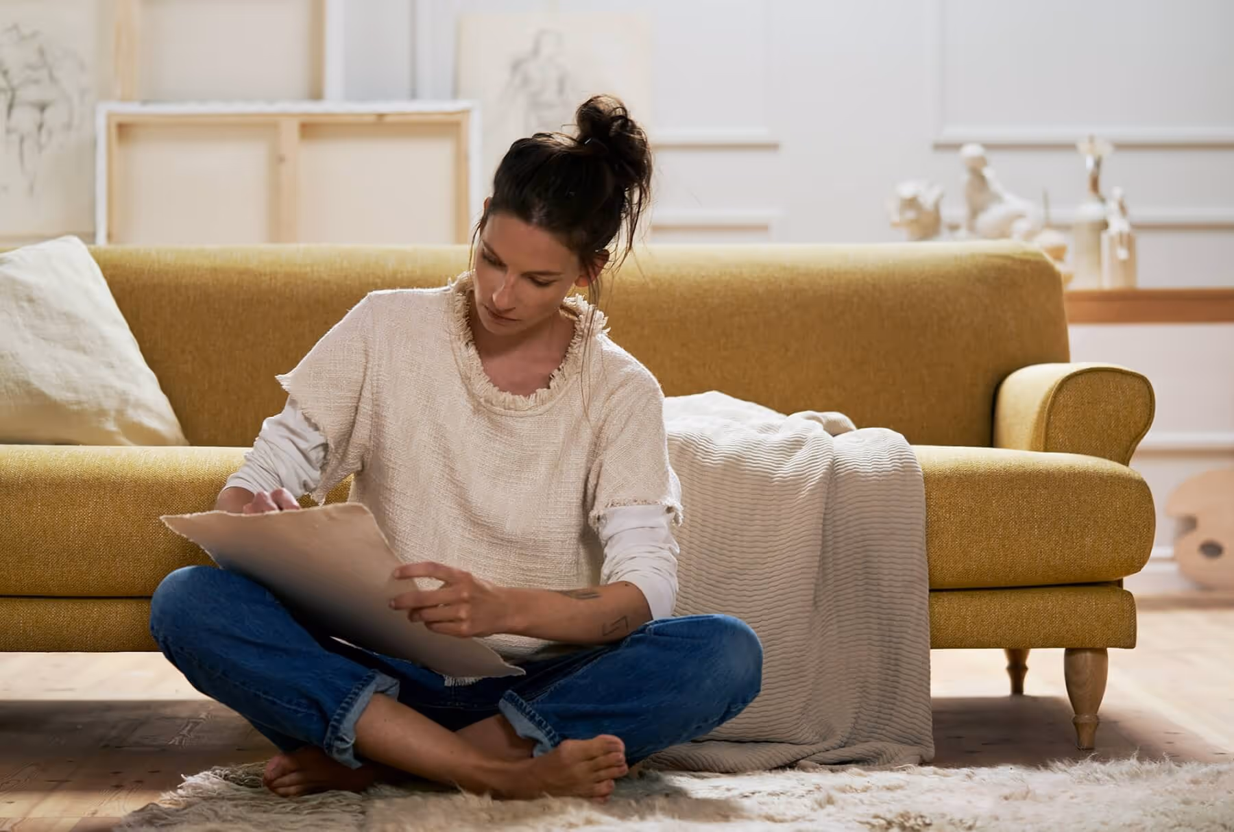 A woman sitting on the floor infront of a sofa writing on a piece of paper