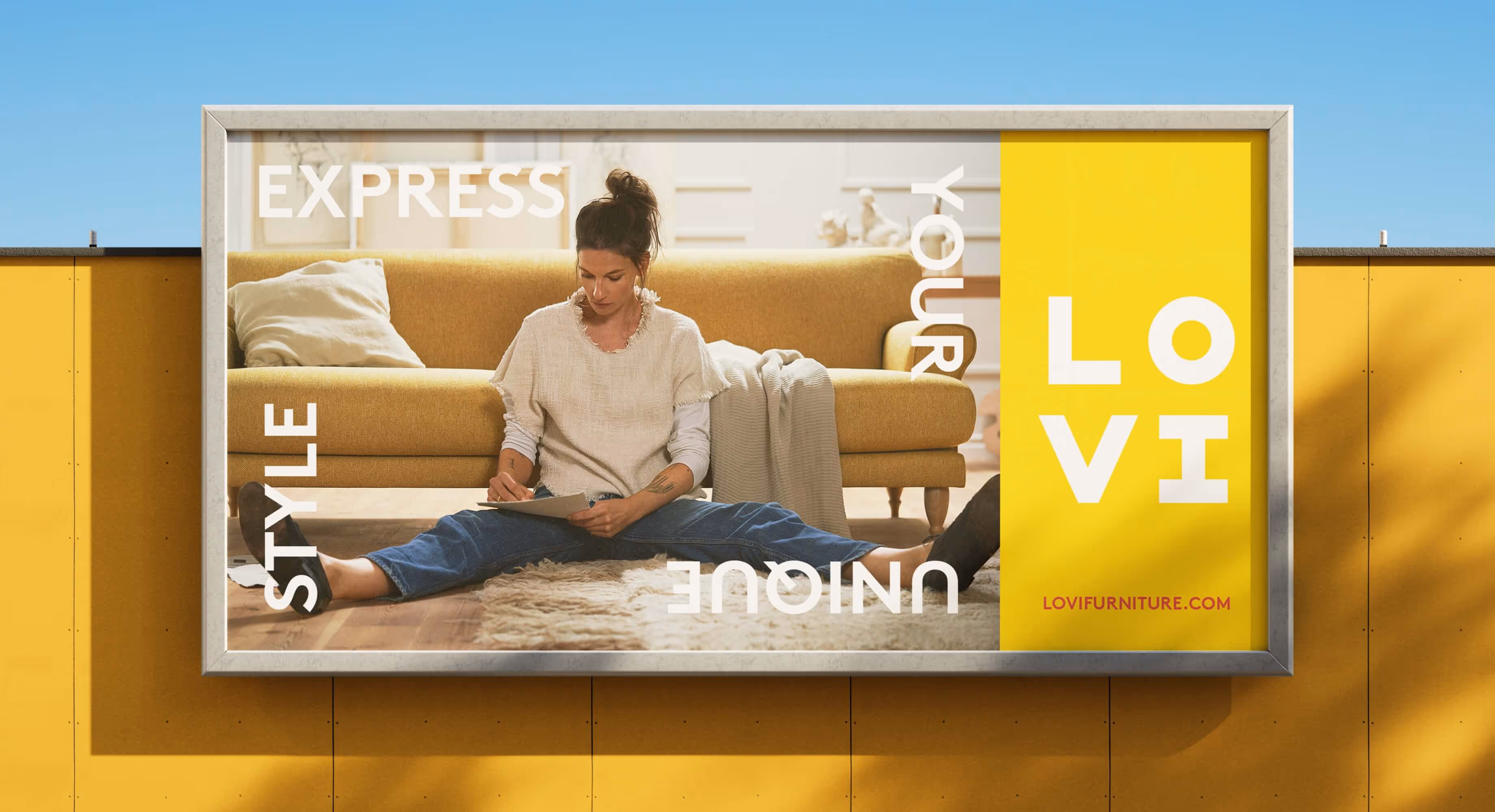 A billboard on a yellow wall with an ad from Lovi with a woman sitting on the floor infront of a sofa writing on a paper