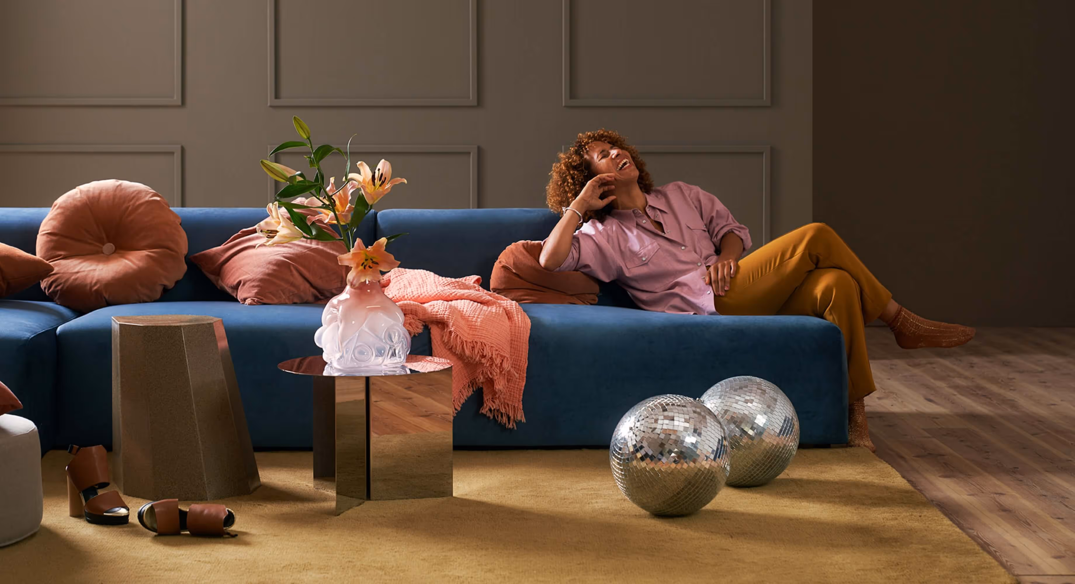 A woman sitting in a sofa laughing with two disco balls on the floor
