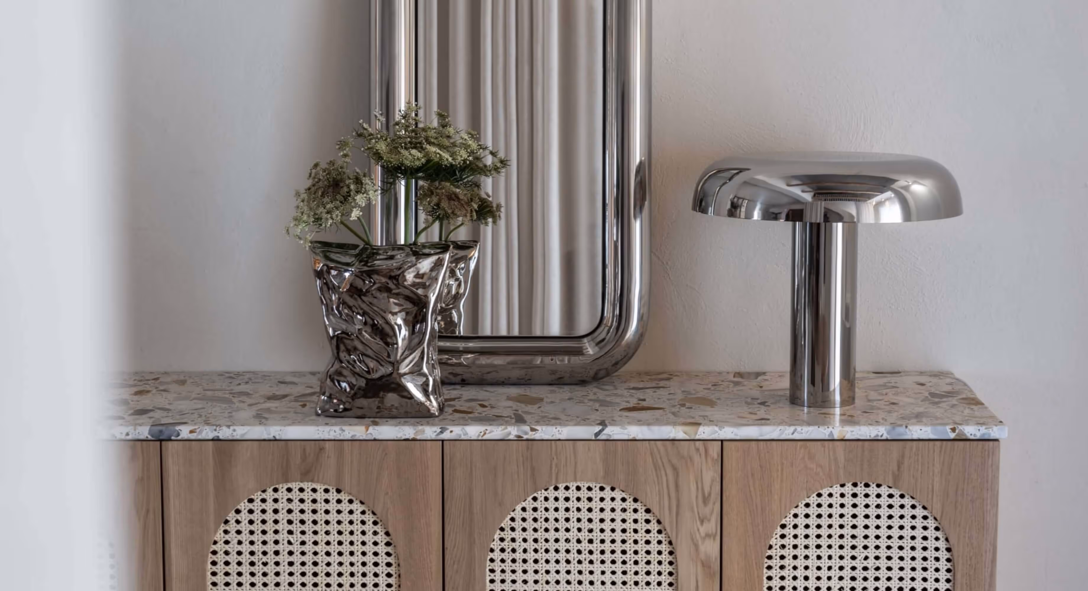 A countertop with a plant, a lamp and a mirror.
