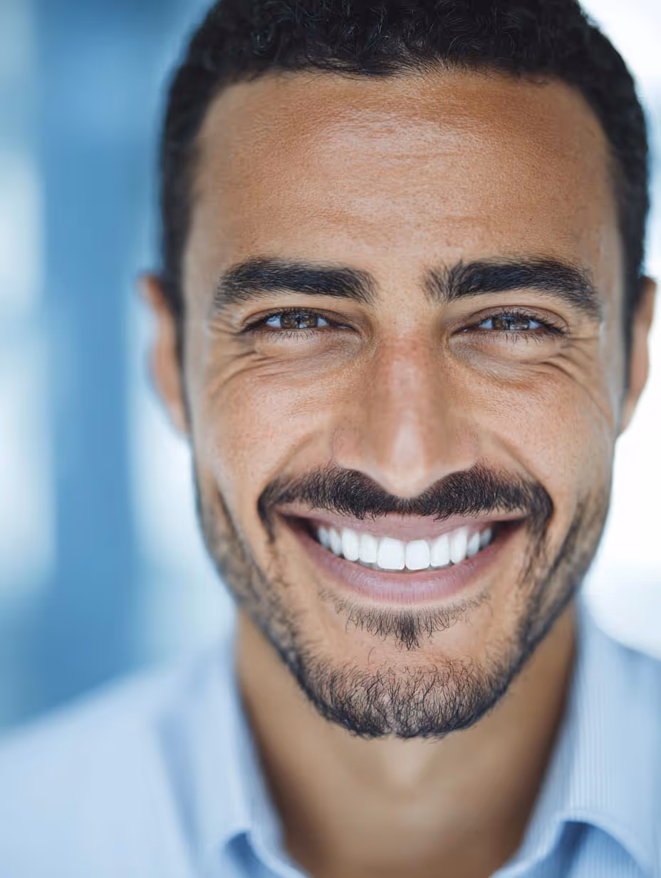 Gros plan sur un homme souriant avec une barbe fine et des dents blanches éclatantes.