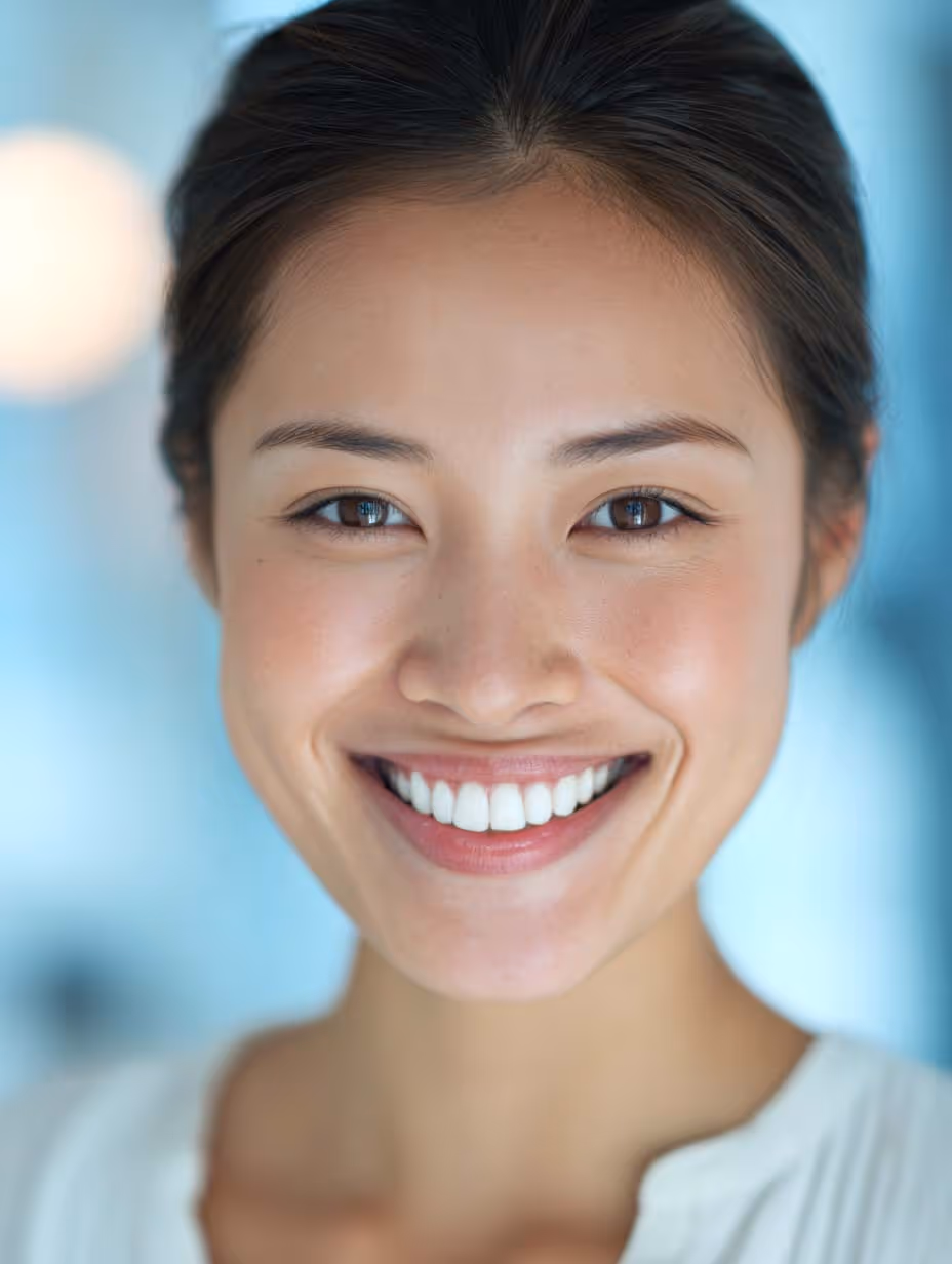 Portrait d'une femme asiatique souriante avec des dents blanches et un fond bleu flou.
