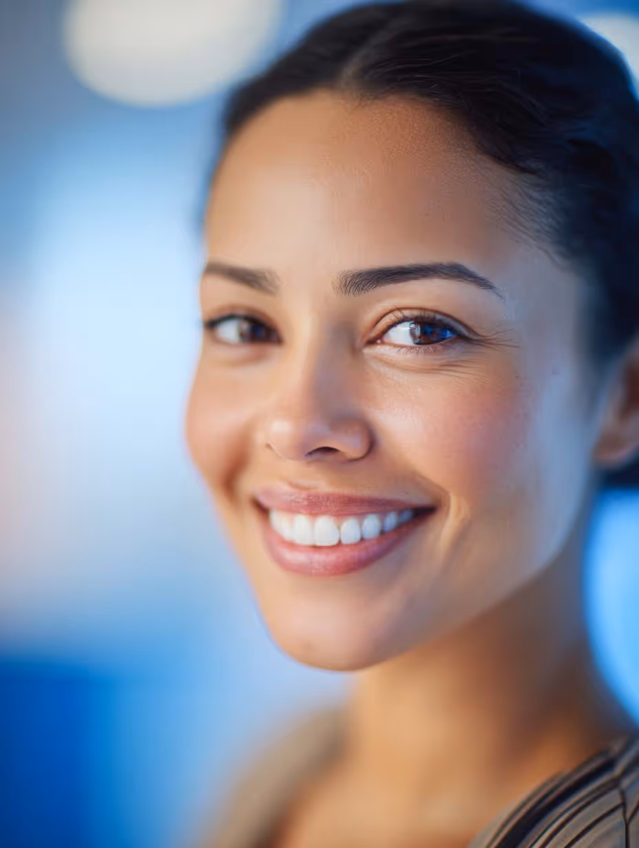 Portrait d'une femme souriante avec une peau lisse et un fond flou bleu.