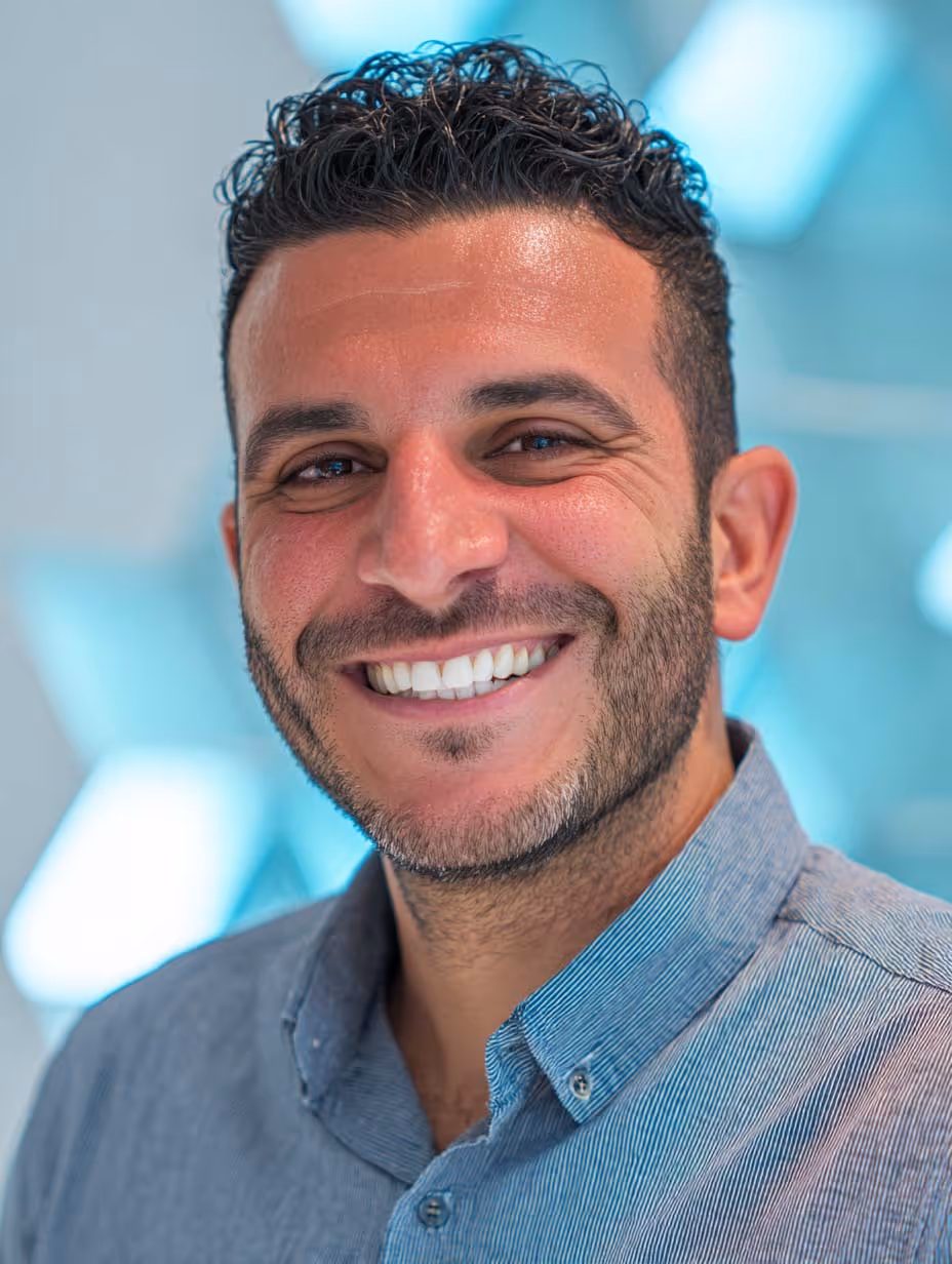 Portrait d'un homme souriant aux cheveux courts et bouclés, portant une chemise bleue et avec un fond flou bleu clair.